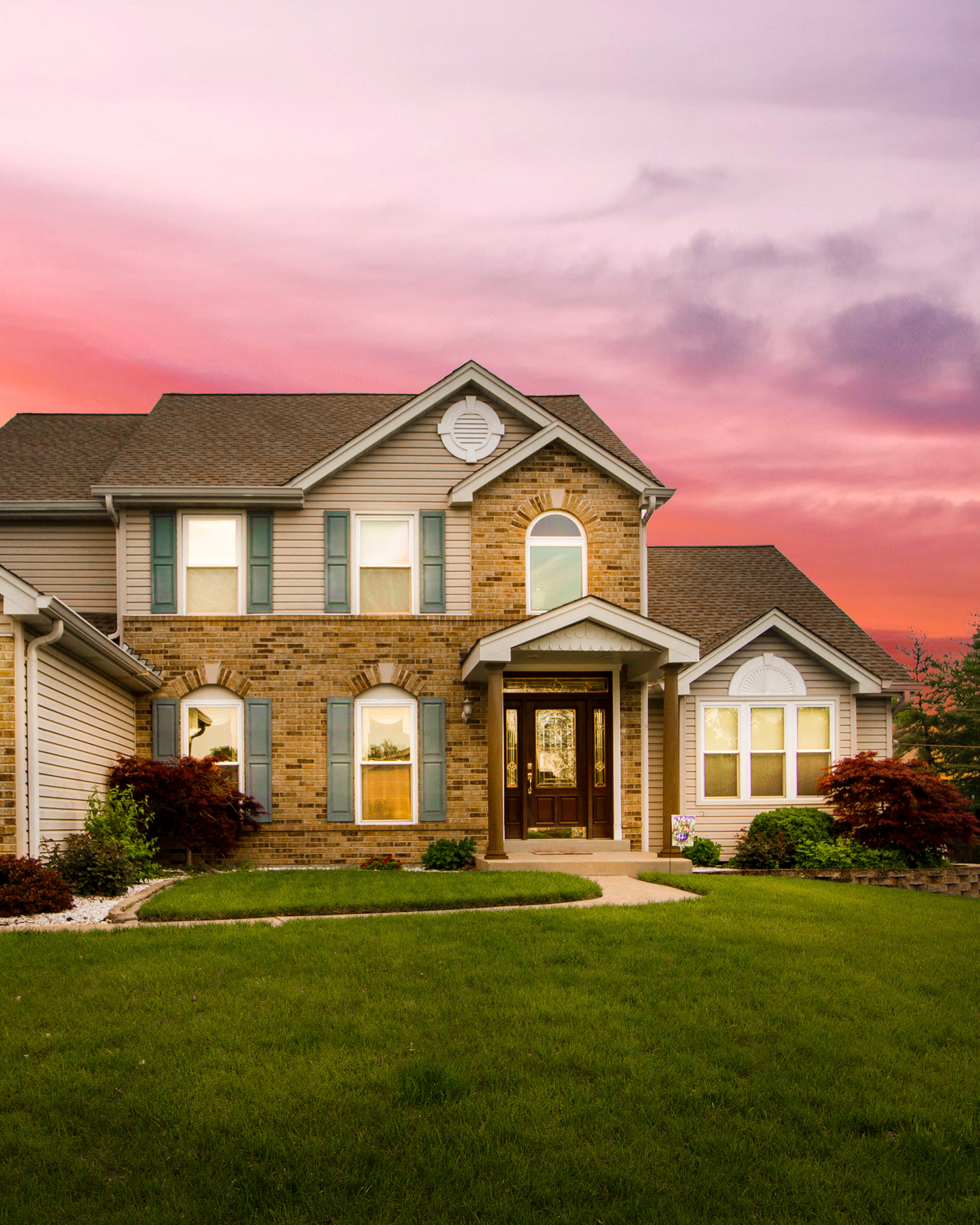 A sequence of luxury suburban homes with stone and vinyl siding facades against a dramatic pink and purple sunset sky.