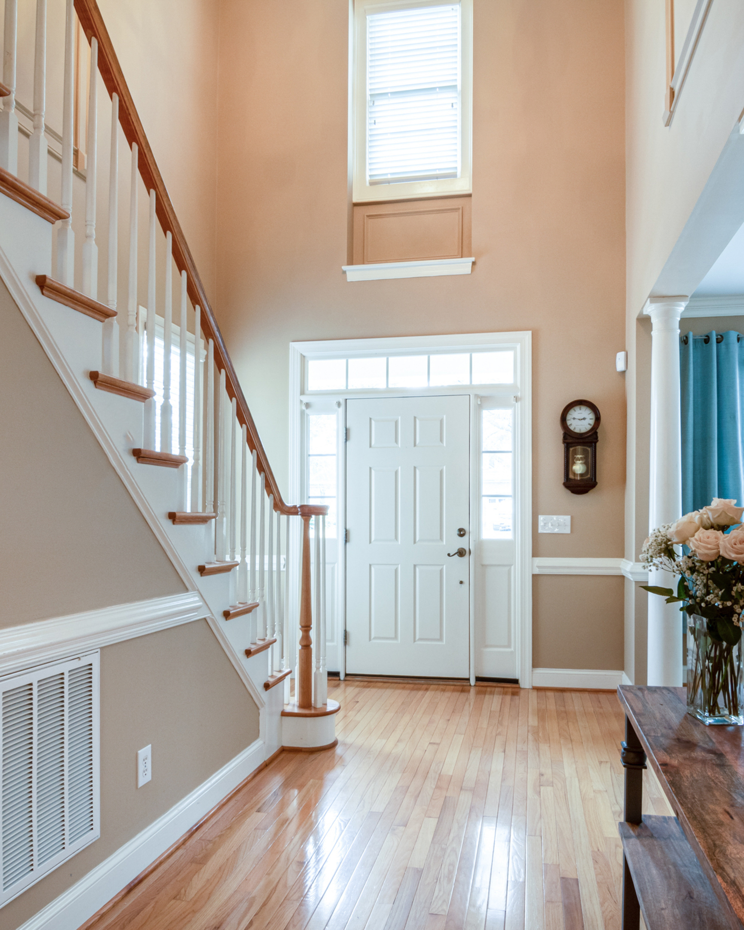 Bright entryway with two-story foyer featuring hardwood floors, white staircase with wood railings, and transom windows.