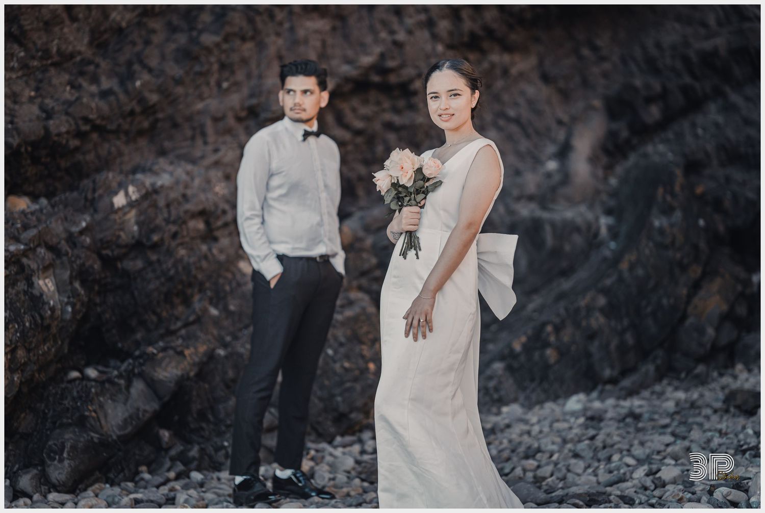 A couple poses for a wedding photo against dramatic rocky coastal cliffs.