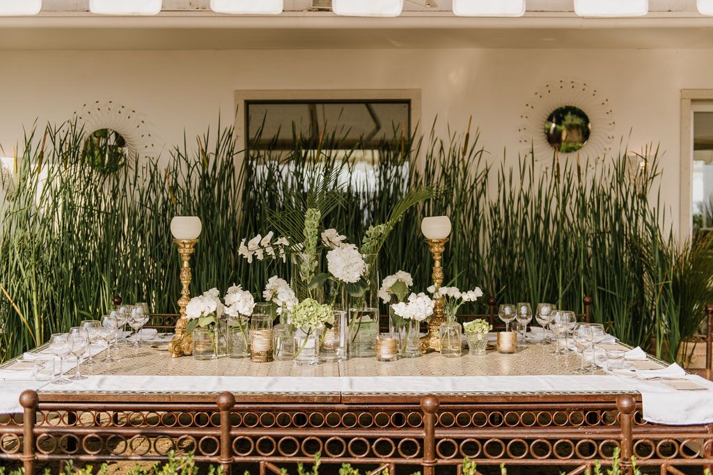 Elegant wedding reception table settings with glowing pendant lights and natural greenery decorations in an indoor venue.