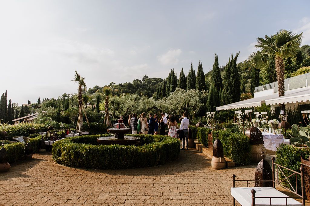 Panoramic view of a Mediterranean-style venue with cypress trees and stone pathways.