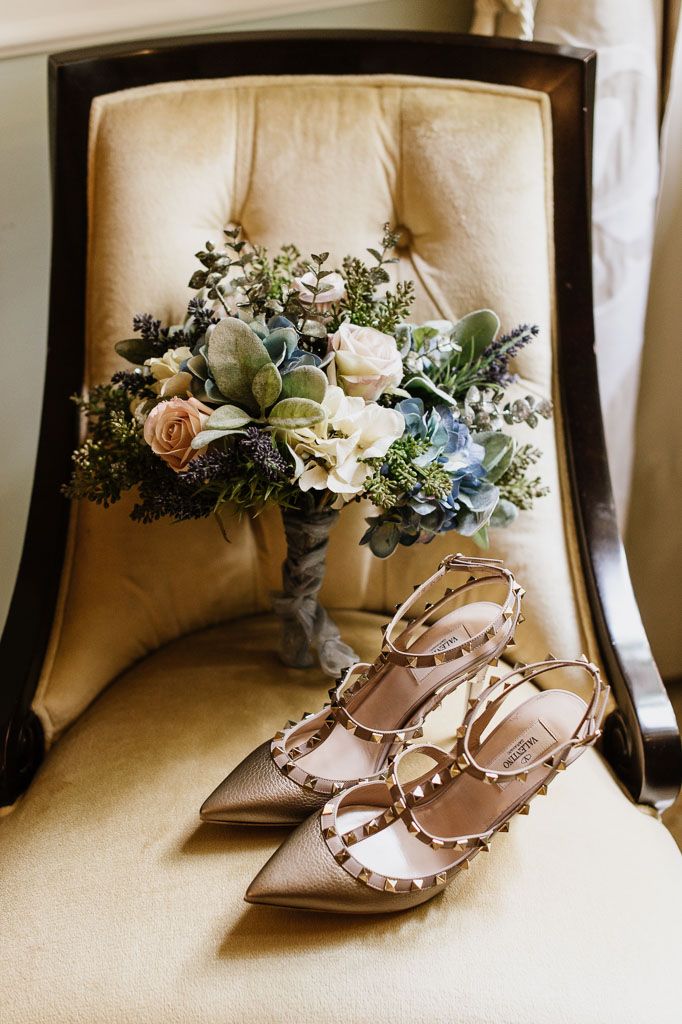 Elegant blush pink Valentino Rockstud heels with floral crown displayed on cream colored chair.