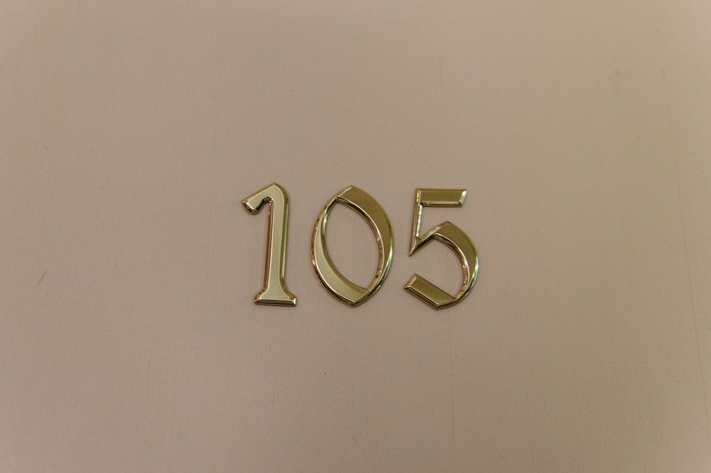 Tan beige numbers painted on wall in a rounded calligraphy font style with distressed texture.
