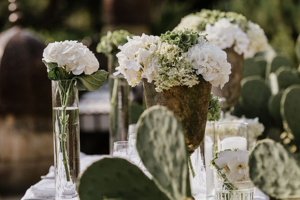 Elegant white floral centerpieces in glass vases adorn tables at an upscale event venue.