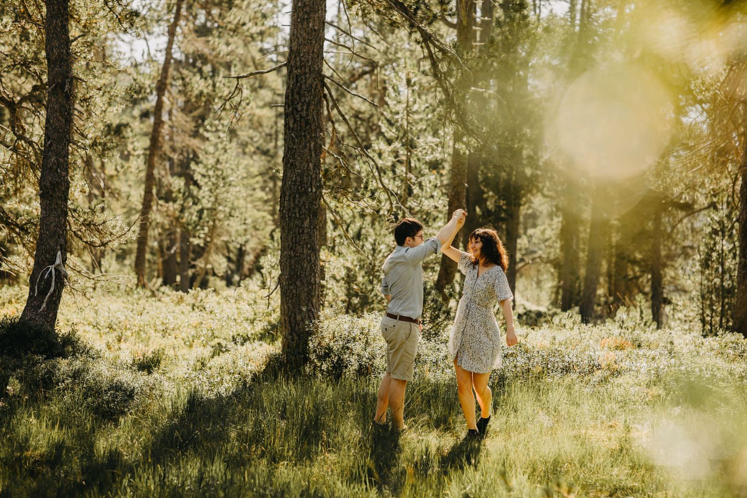 Dancing in sunlit forest clearing during summer engagement session.