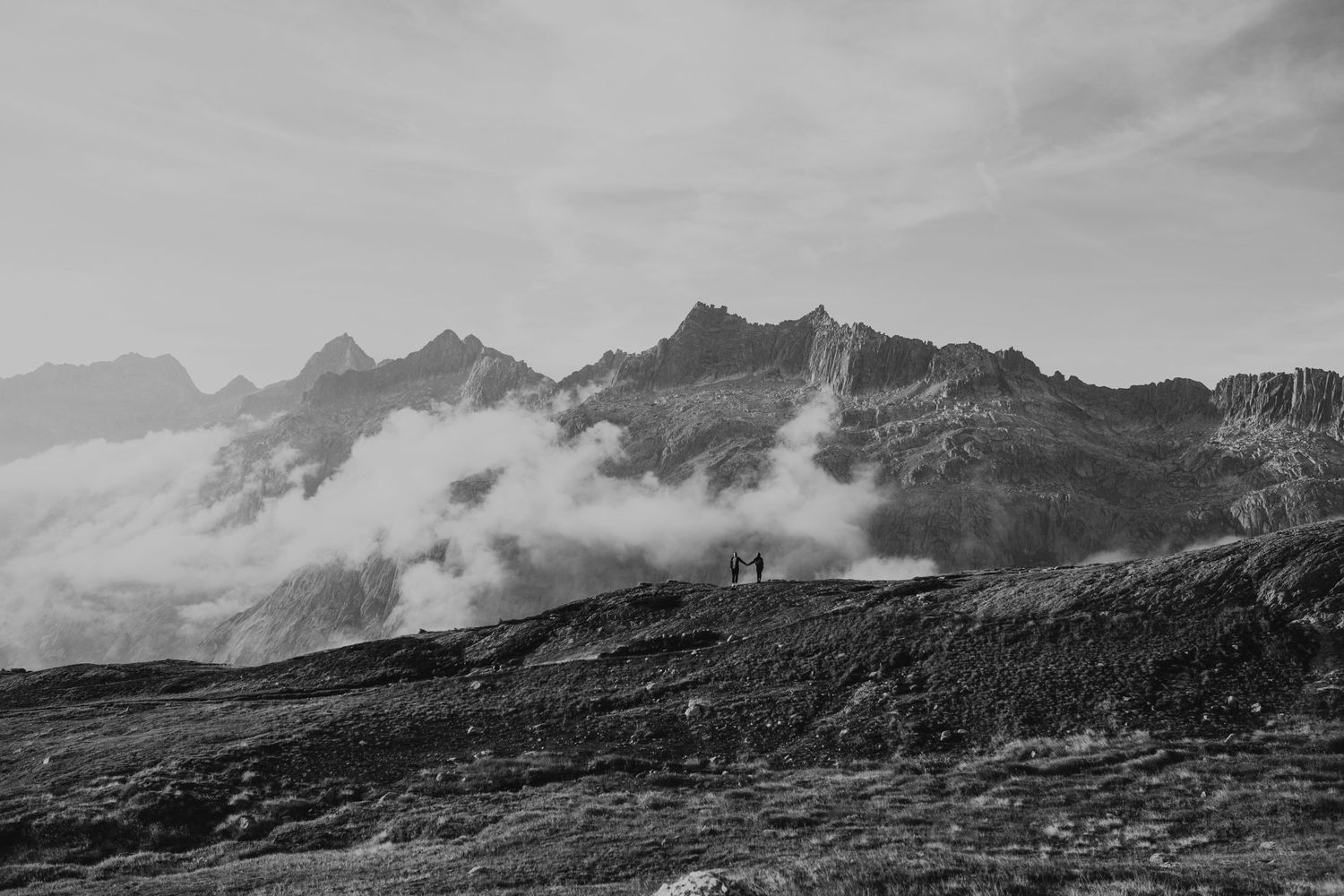 Black and white landscape of misty mountain peaks with silhouettes on ridge.