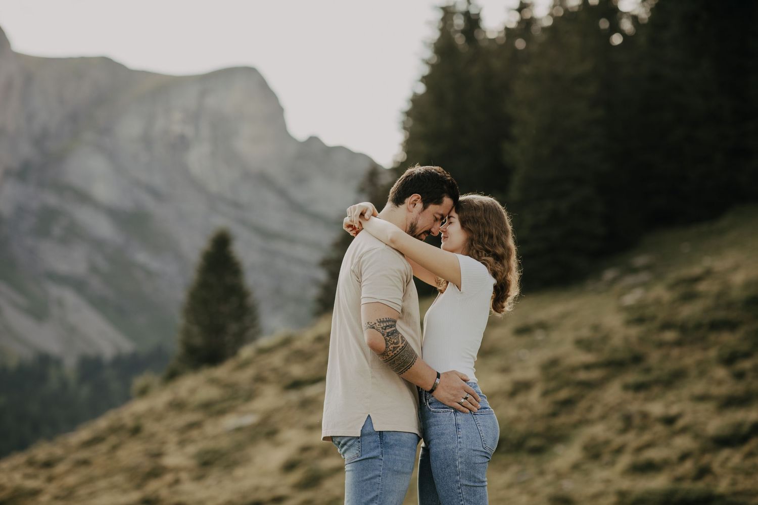 Romantic embrace between two figures on a mountain hillside with dramatic peaks in the background at golden hour.