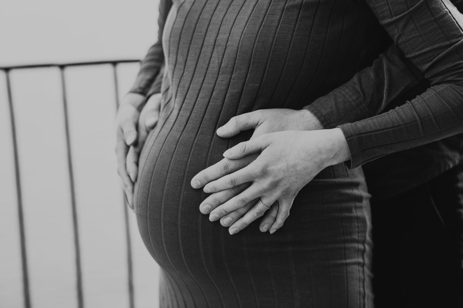 Black and white close-up of hands gently cradling a pregnant belly.