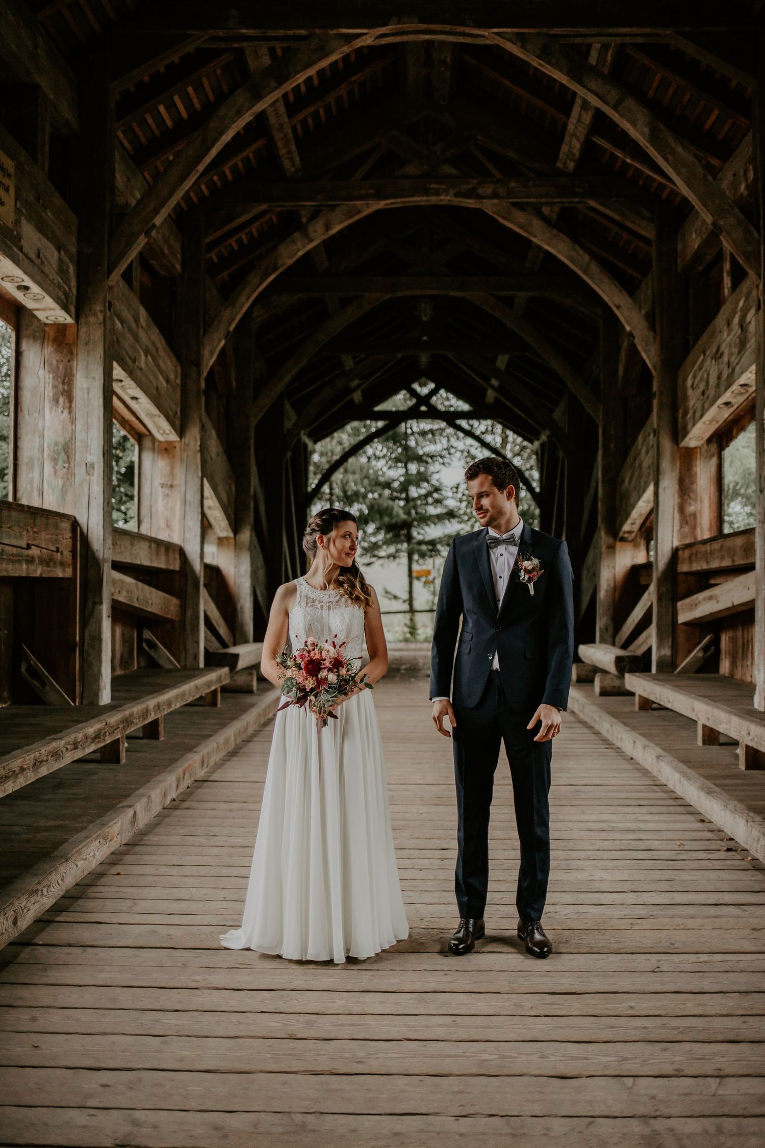 Newlyweds standing in rustic wooden covered bridge for wedding portrait.