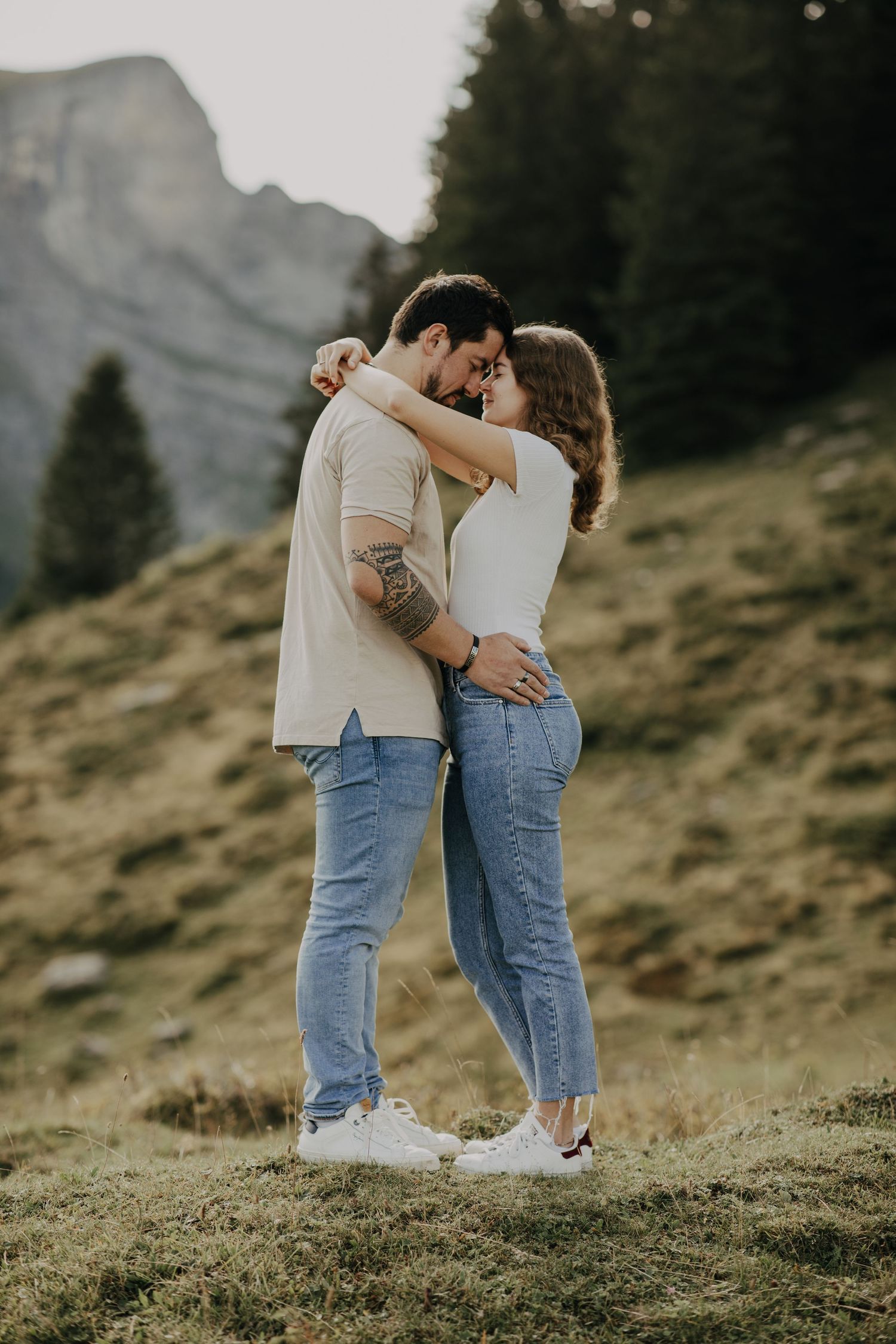 A romantic couple embraces on a mountainside during golden hour.