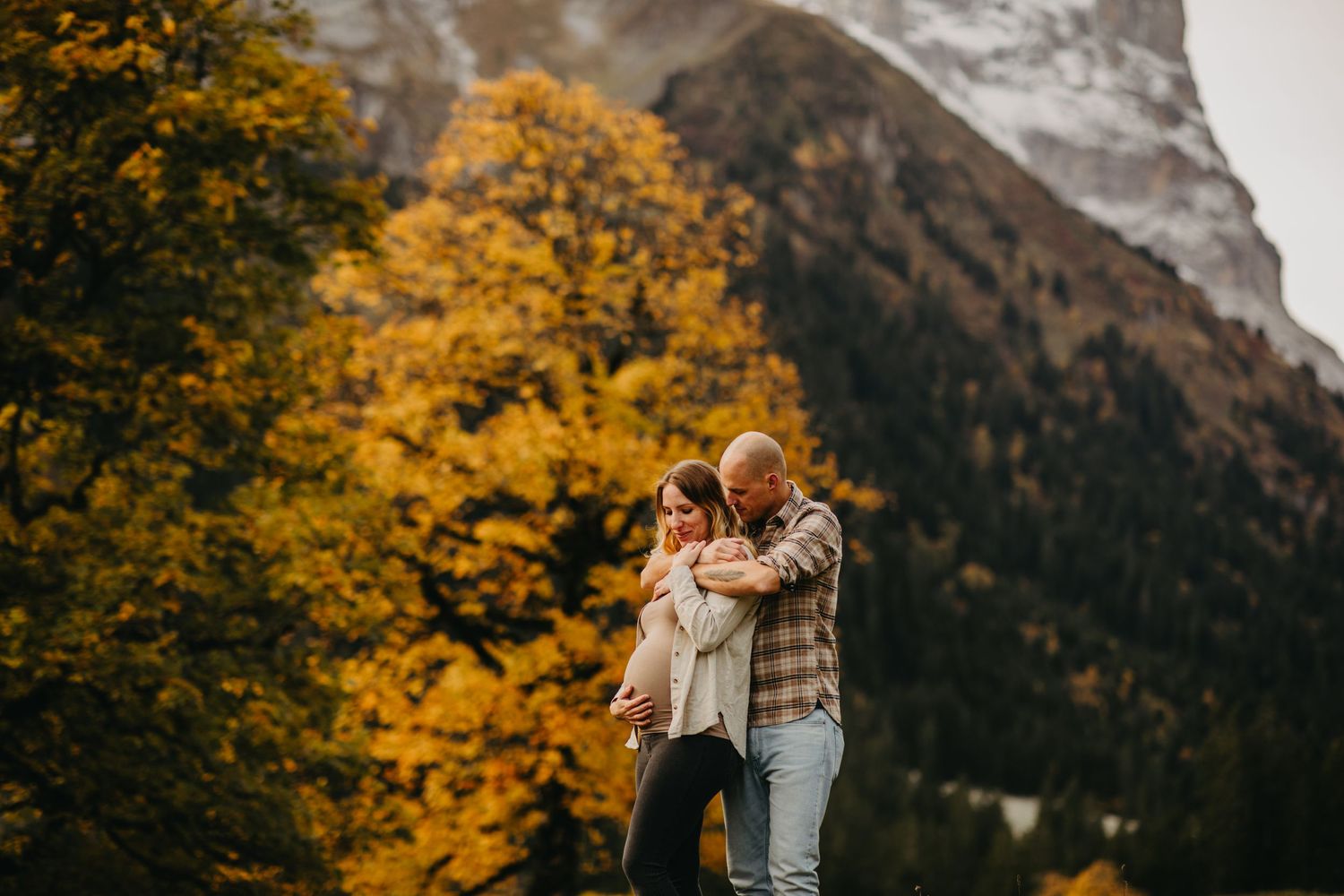 Couple embracing with autumn foliage and mountain backdrop in warm evening light.