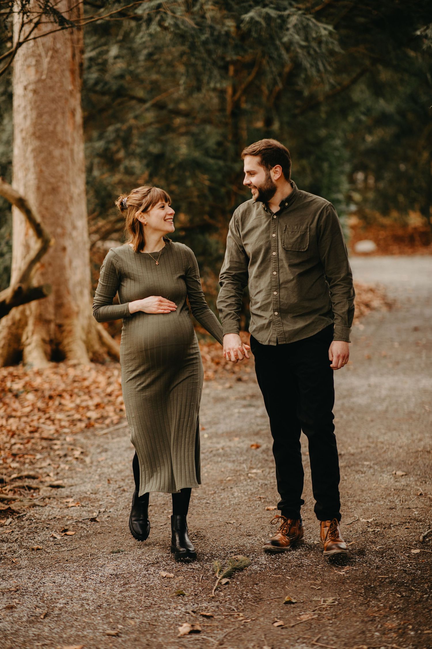 Expectant couple walking on autumn forest trail with fallen leaves.