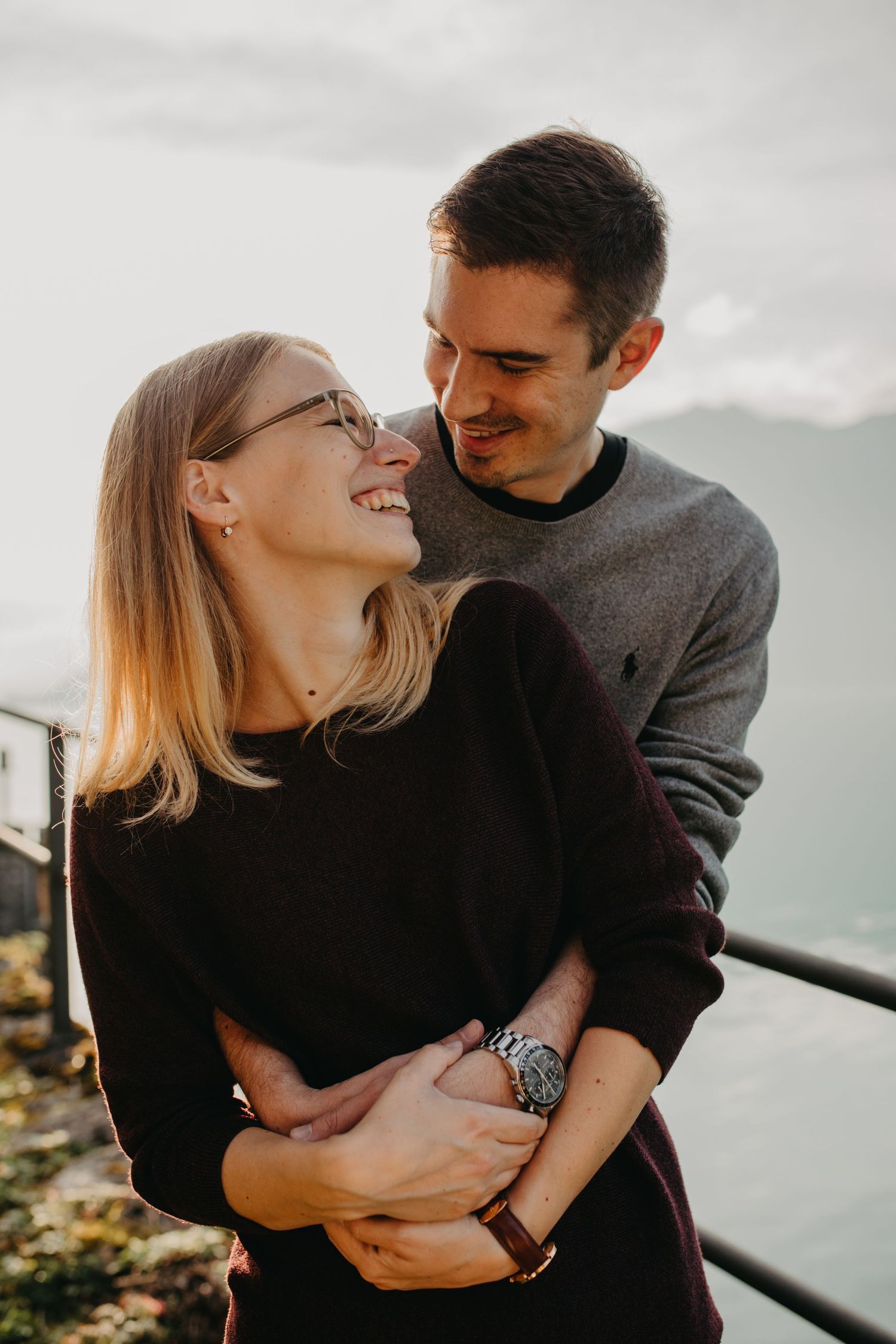 Couple in matching dark sweaters sharing romantic moment at sunset overlook.