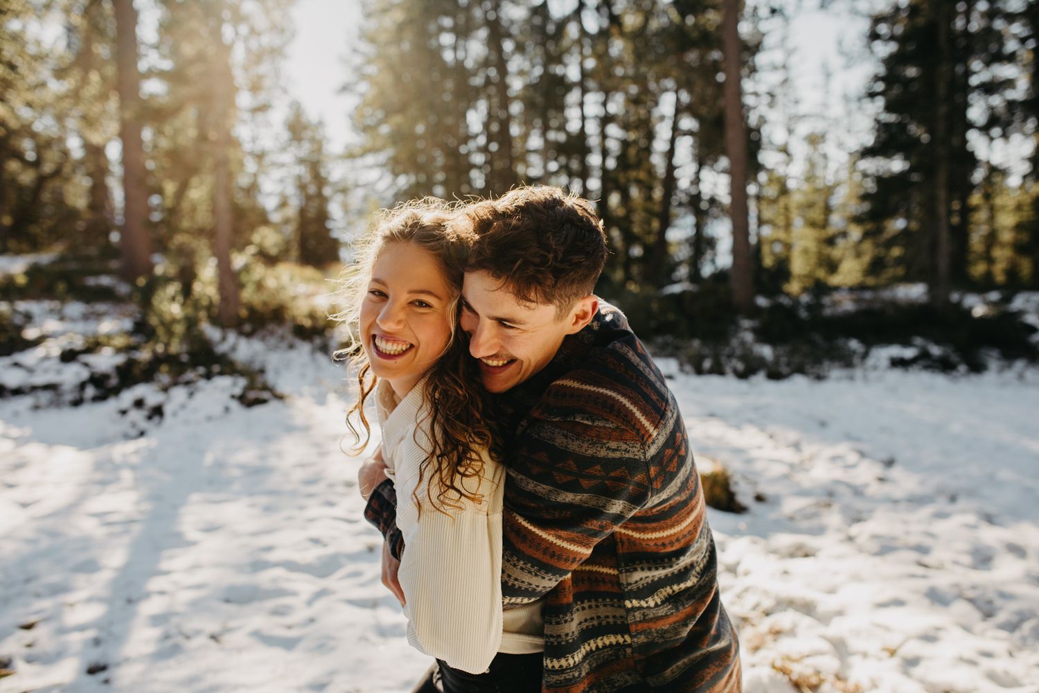Playful moment captured in snowy winter forest with sunlight streaming through pine trees.