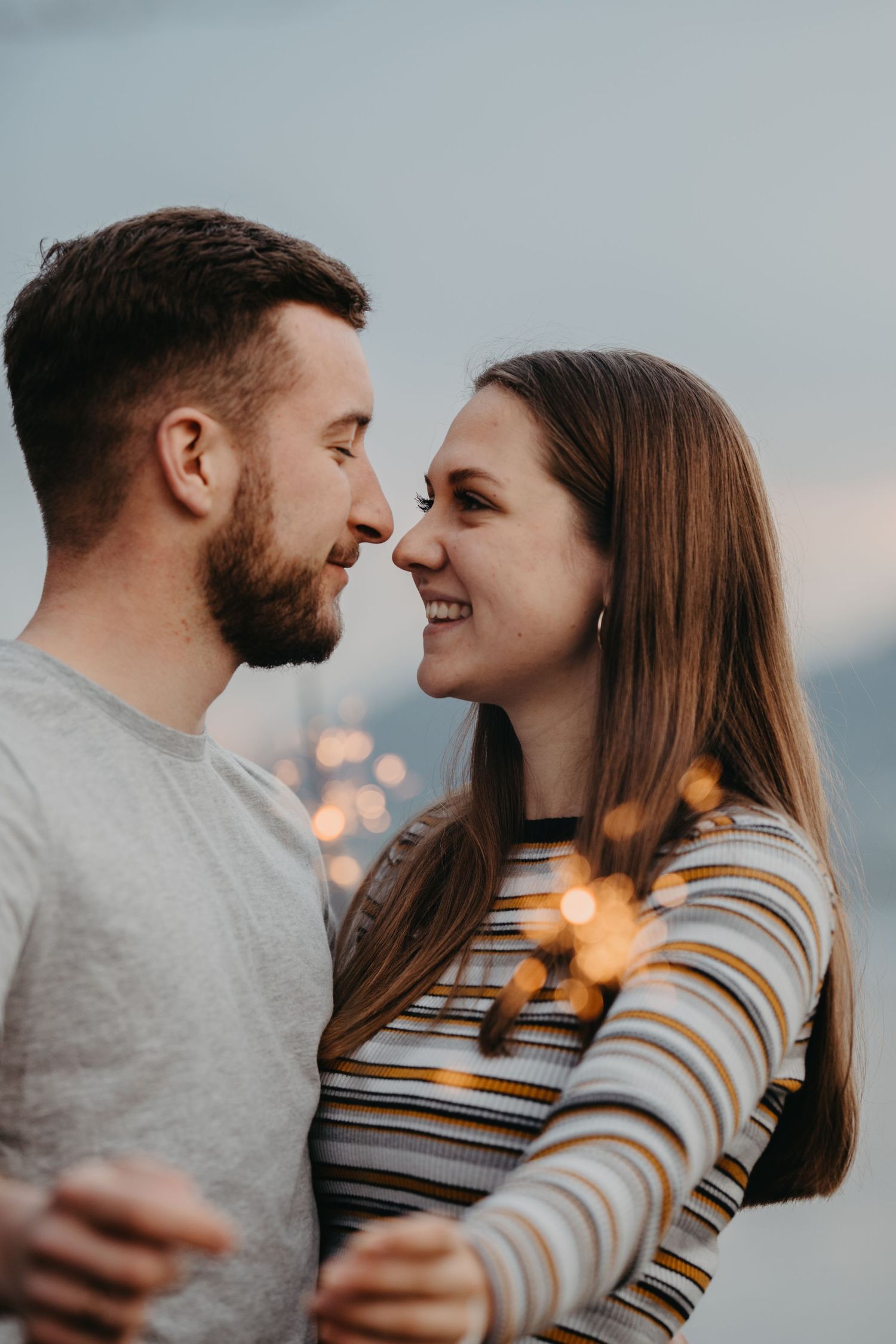 An intimate couple sharing a joyful moment at sunset with glowing bokeh lights in the background.