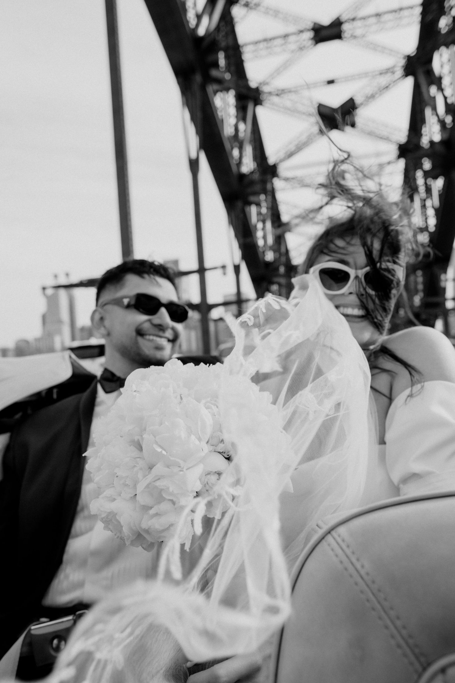 A vintage-style black and white wedding photo of a couple wearing sunglasses in a convertible.