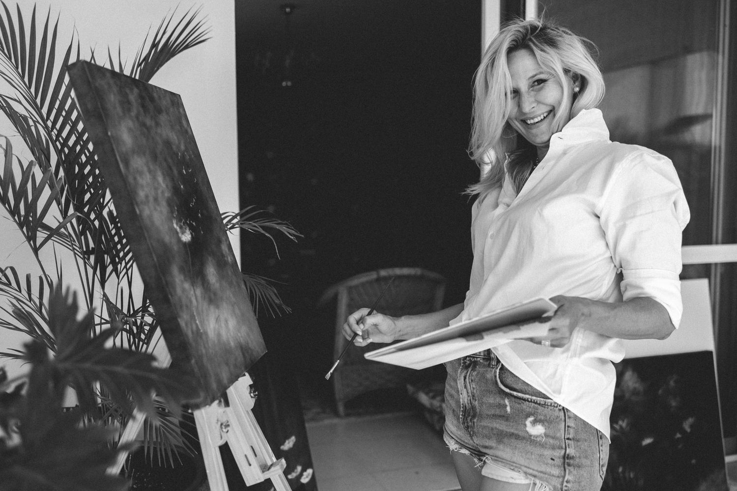 A person wearing a white button-down shirt sits in an outdoor setting with palm plants and dark lighting.