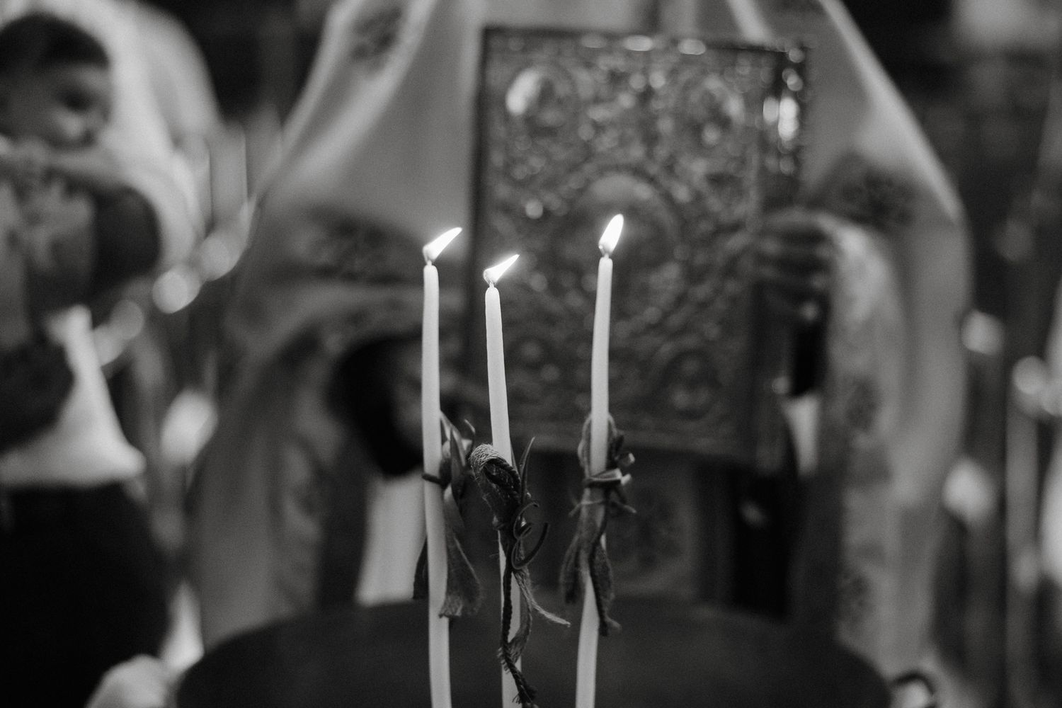 Black and white photo of three lit candles in a church during an Orthodox Christian religious ceremony.