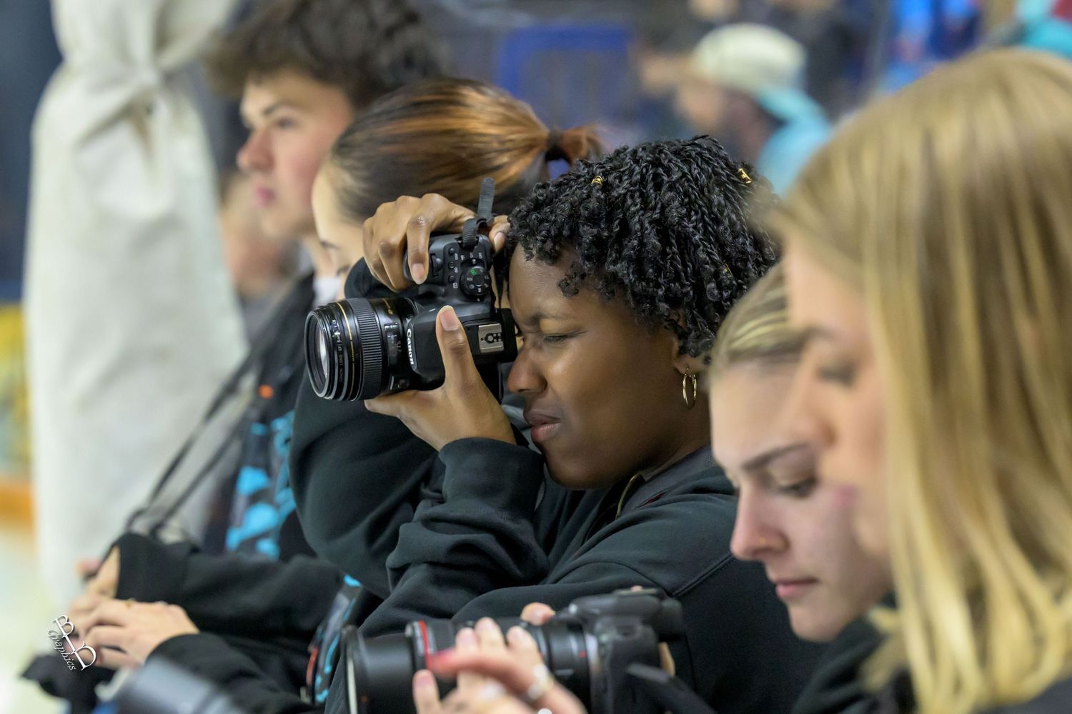 Photographers with professional cameras focus intently while seated in a row at an event.