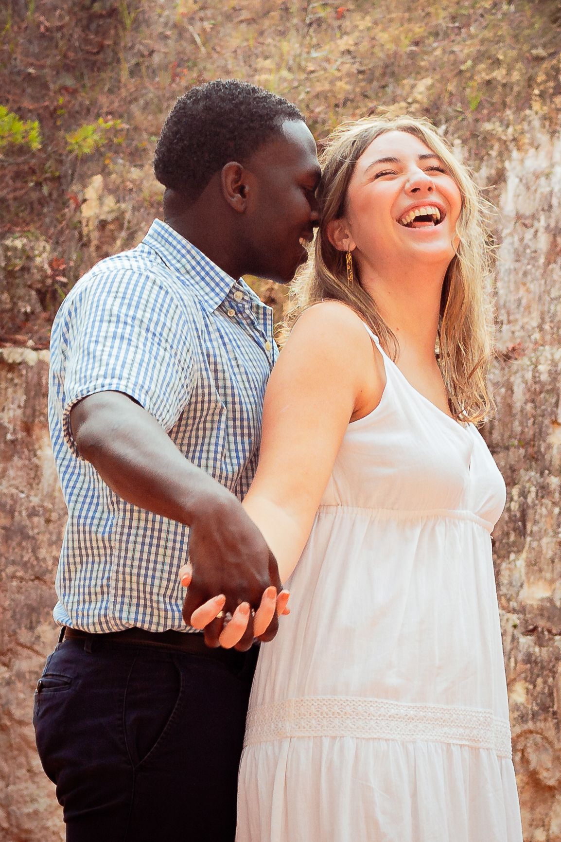 A joyful couple shares a tender moment together against a rustic stone wall.