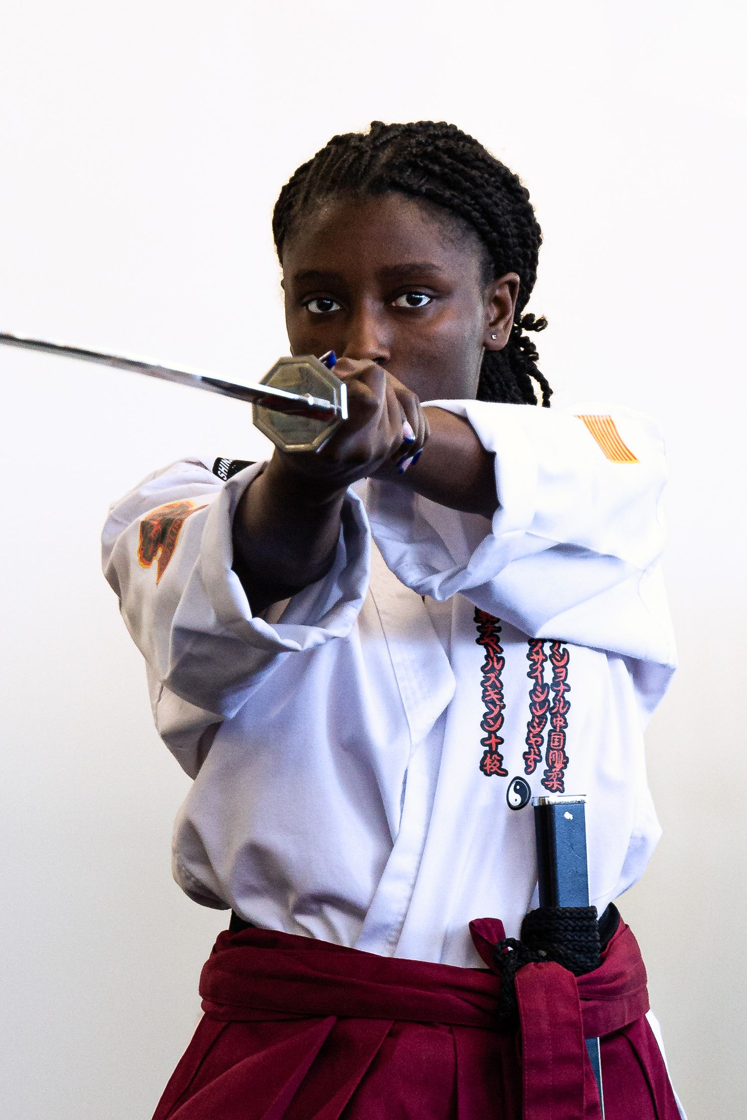A person in karate attire holds a sword in ready position against a white background.