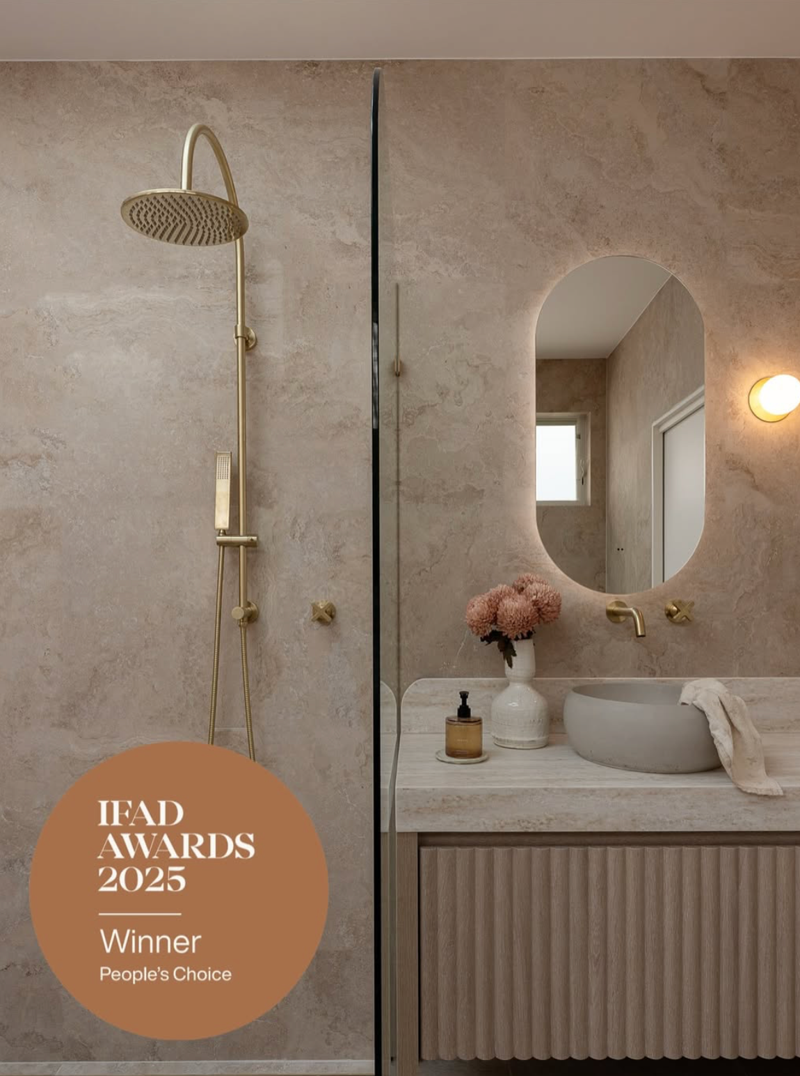 Modern bathroom interior with textured beige walls, brass fixtures, and circular mirror showcasing minimalist design elements.