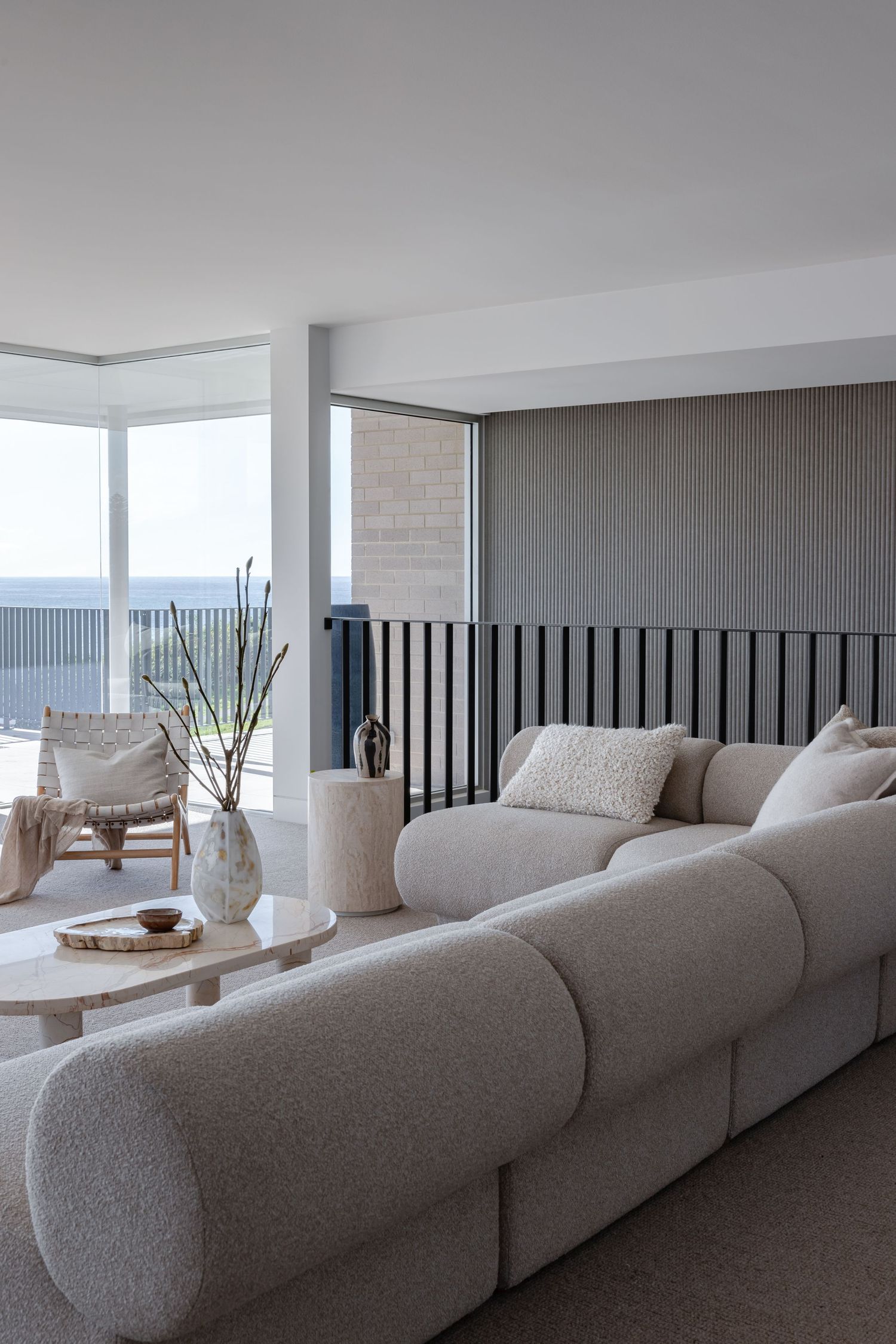 Modern living room features a curved gray sectional sofa with plush cushions and panoramic windows overlooking city views.