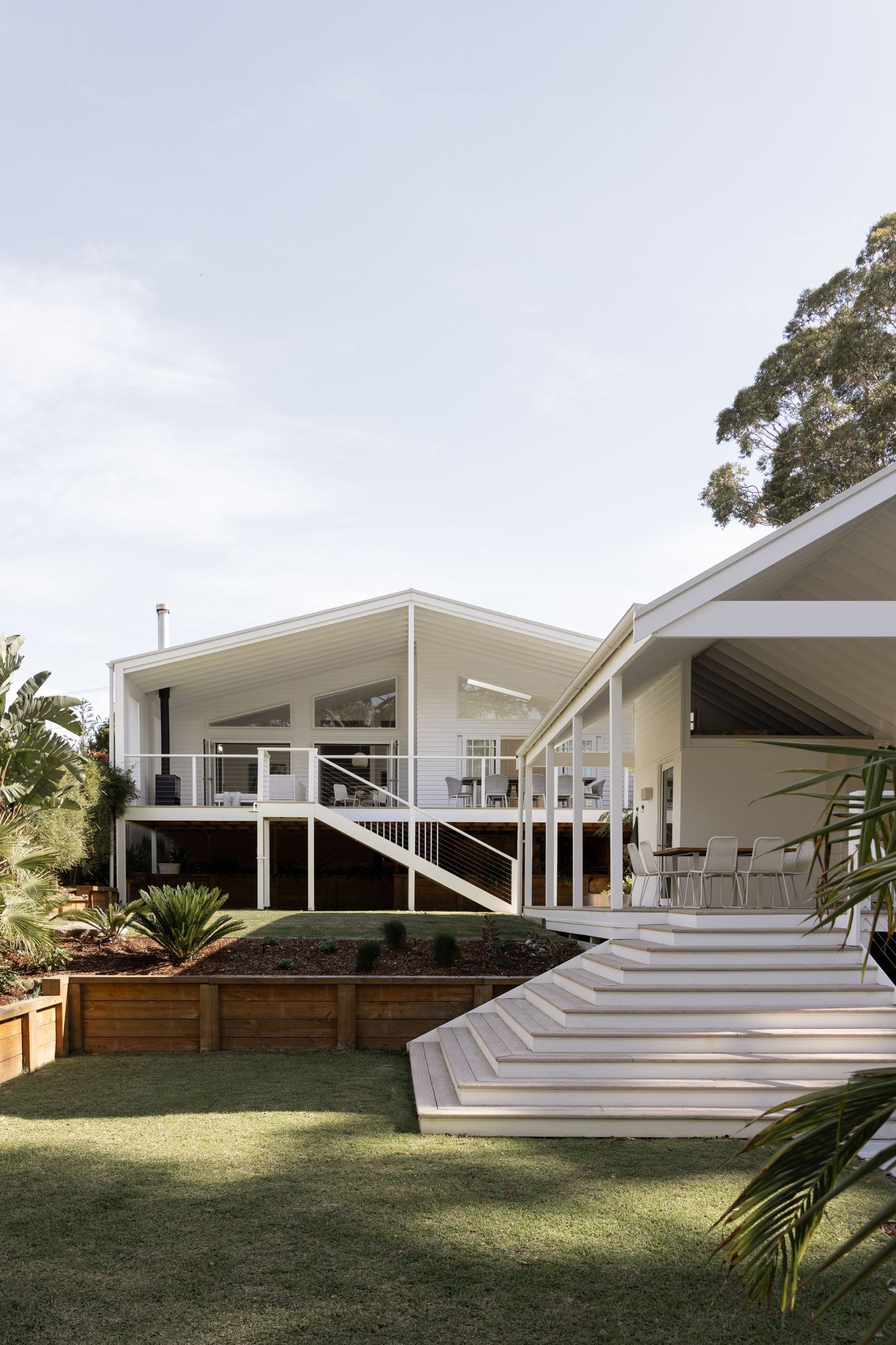 Modern white house exterior features cascading steps and angular architecture with clean lines and landscaped yard.