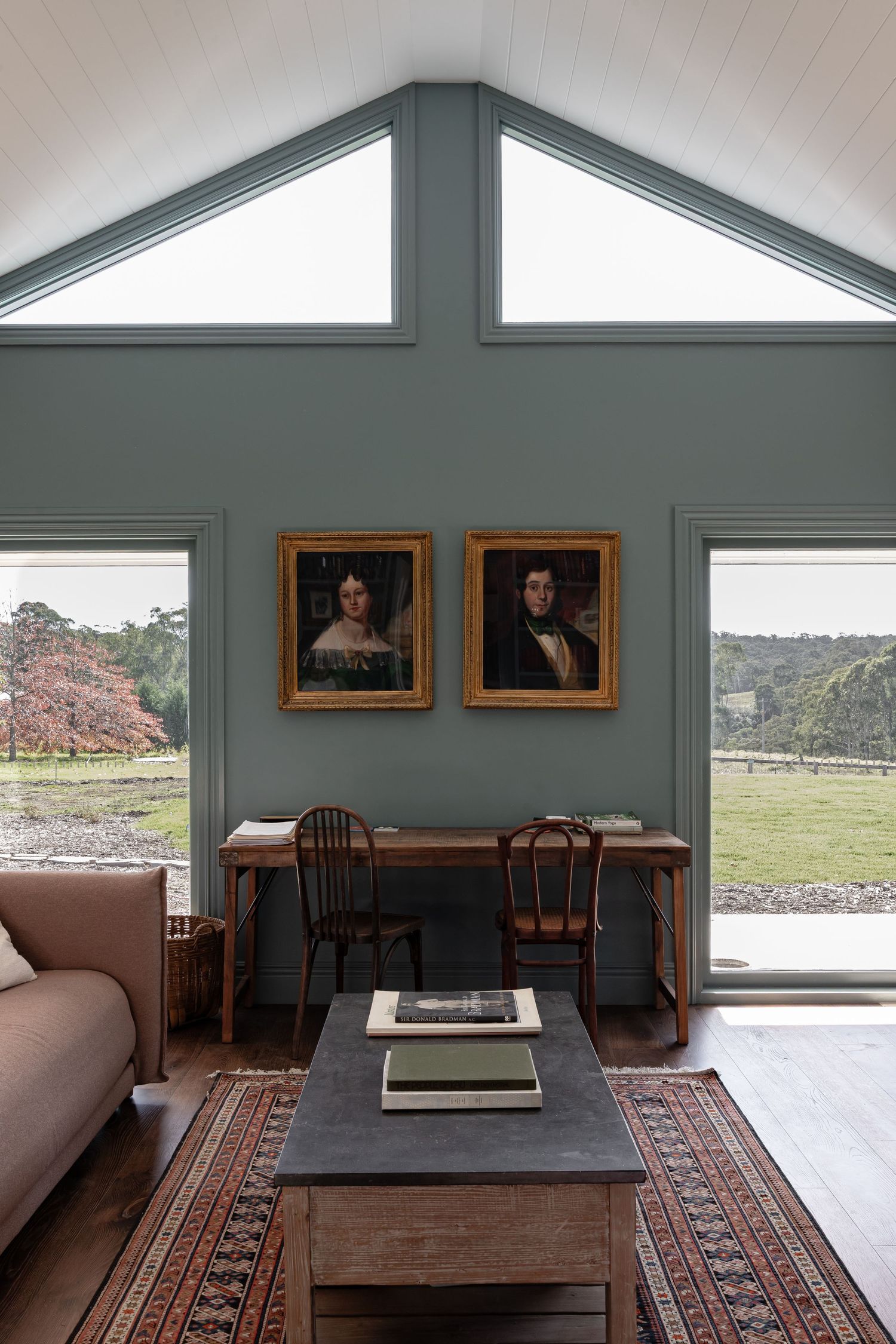 A modern interior space with wood furniture, framed artwork, and large windows offering pastoral views of the countryside.