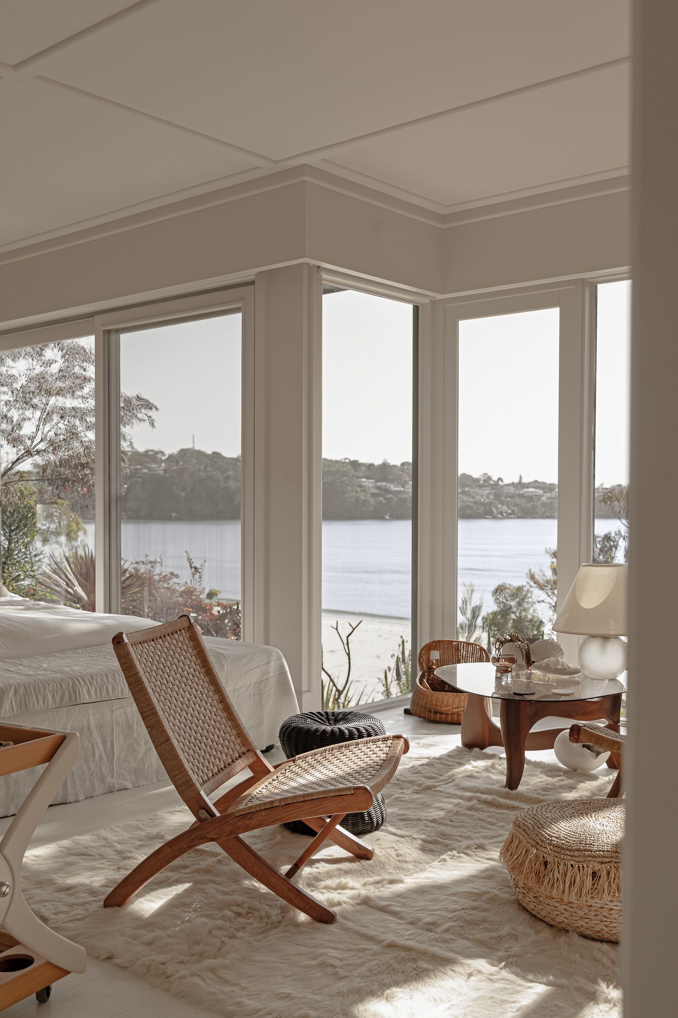 Sunlit waterfront room with wooden lounge chairs and panoramic windows overlooking the bay.