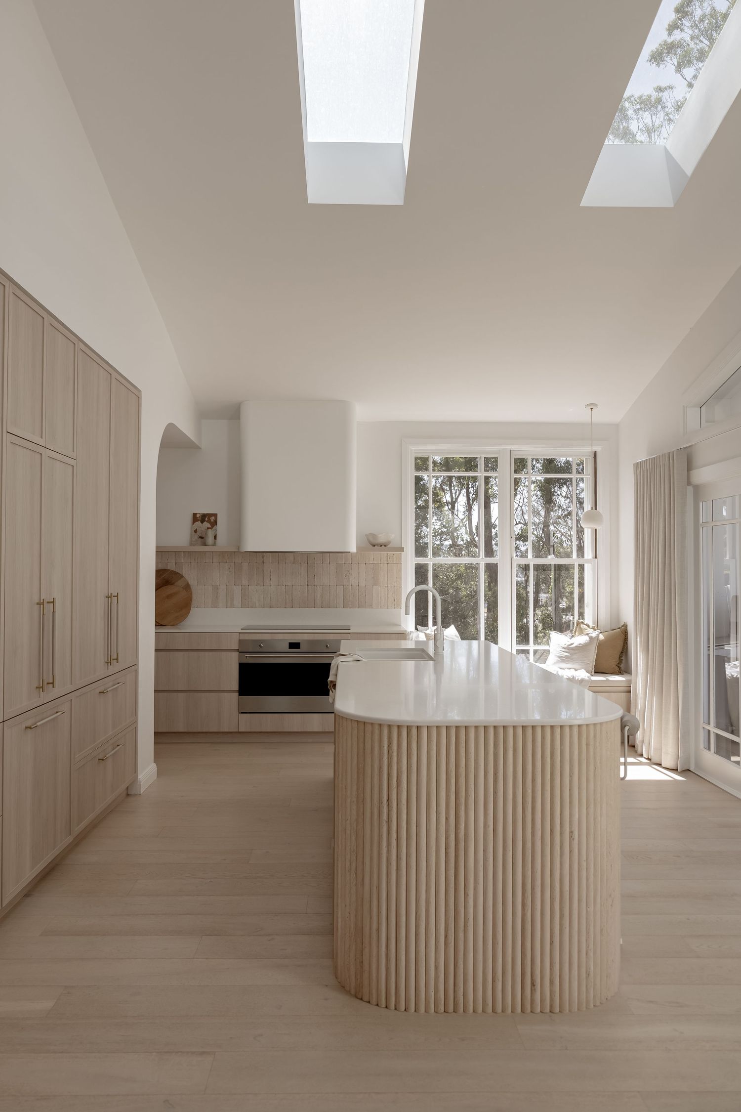 Modern white kitchen with curved island, light wood floors, and skylight windows showcasing minimalist Scandinavian design.