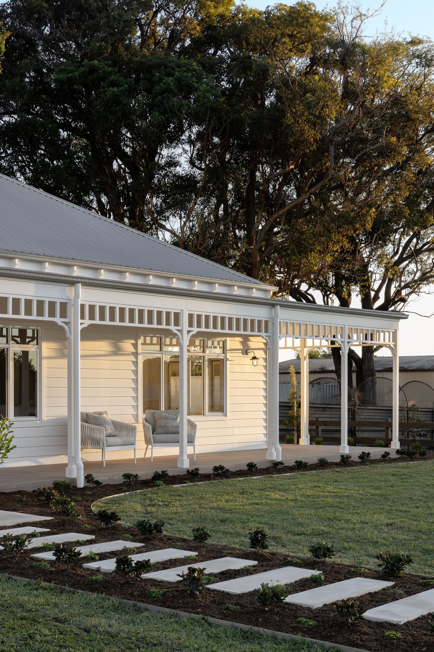 A modern farm house with a covered porch and concrete stepping stones leading through a landscaped lawn.