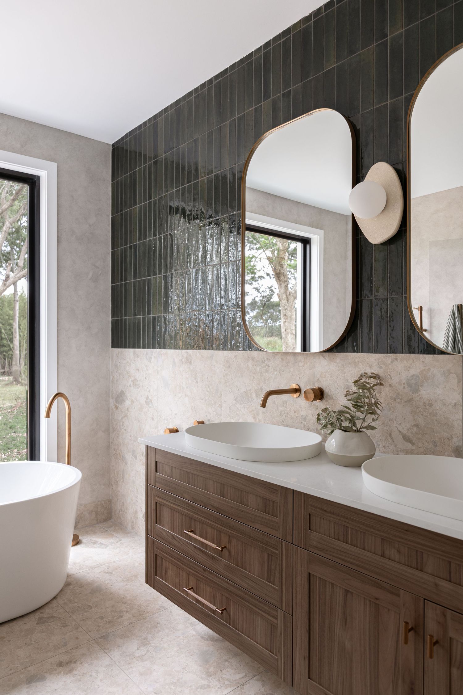 Bathroom that features dark green vertical tiles  and warm , walnut cabinetry with marble countertops.