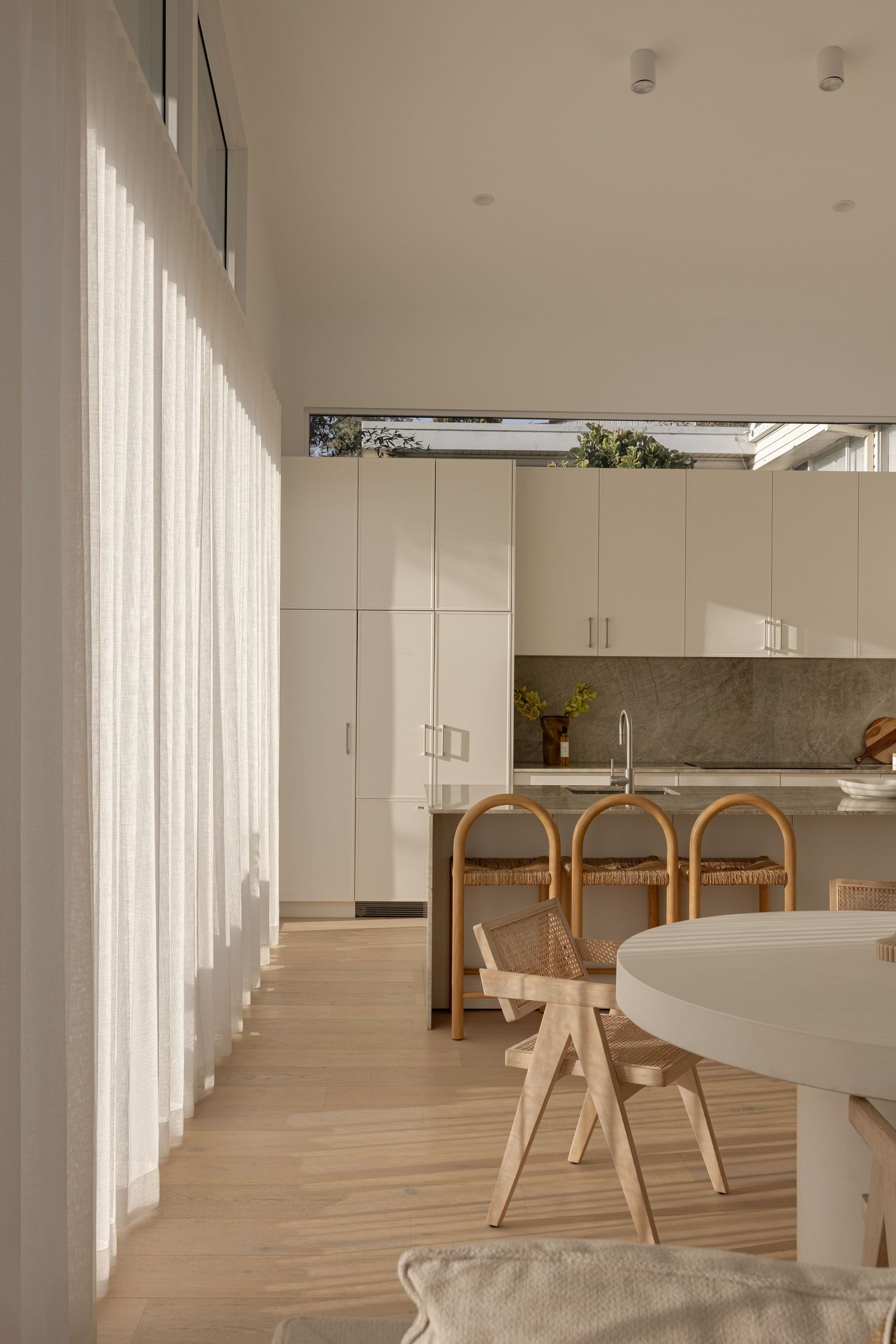 Minimalist dining room with white walls, wooden flooring, and modern furniture in a bright, sunlit space.
