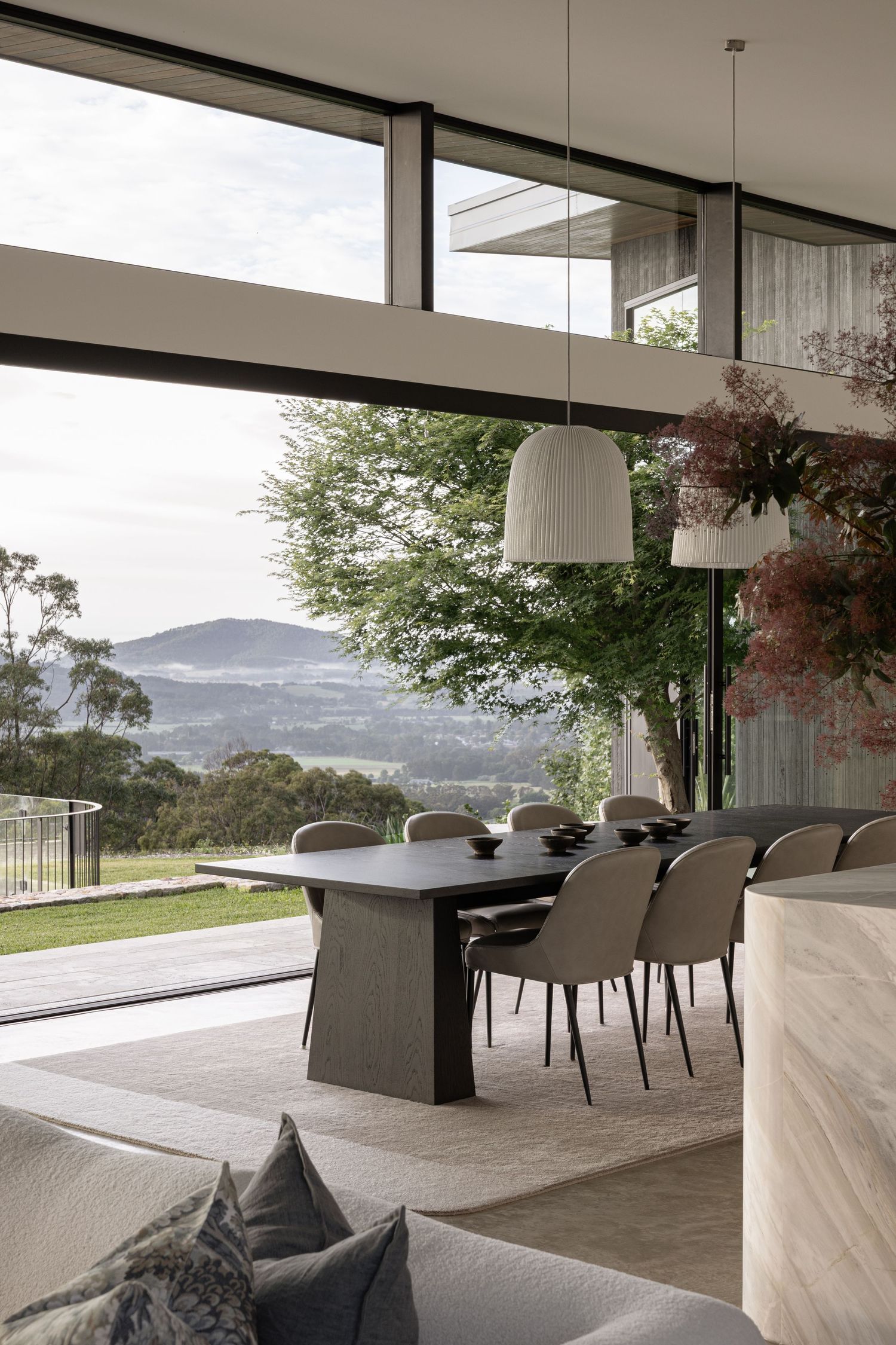 Modern open-concept living room with floor-to-ceiling windows showcasing mountain views and minimalist grey furniture.