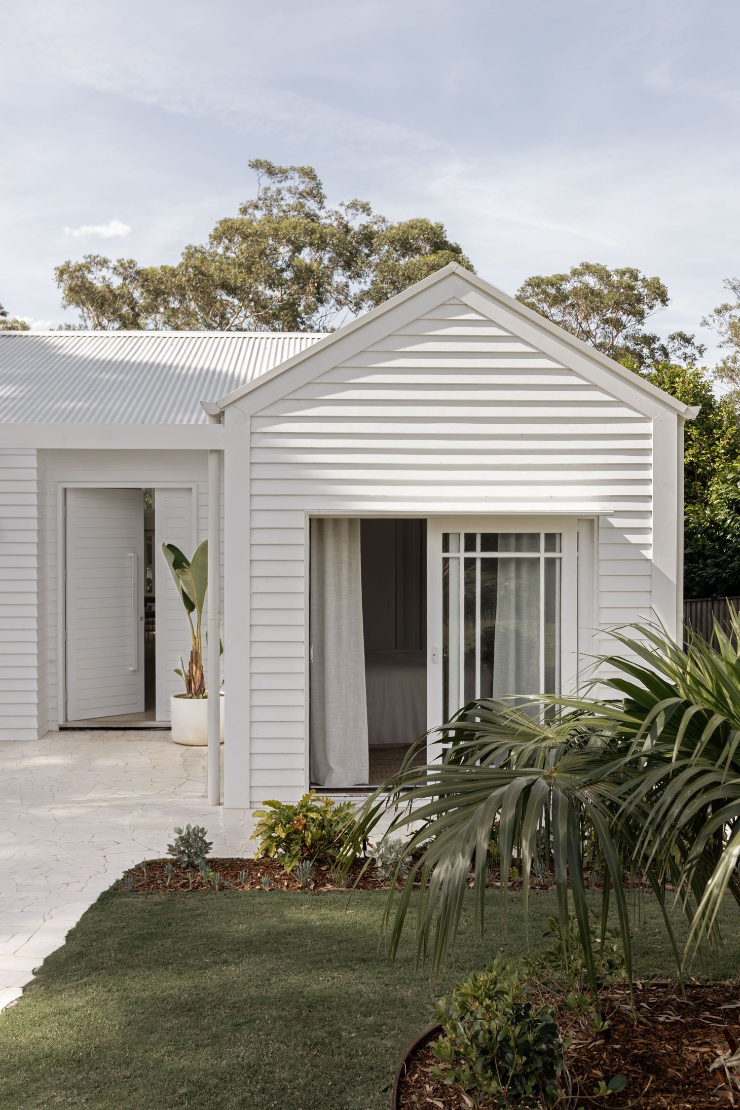 Modern white coastal home exterior with clean lines and tropical landscaping features multiple connected pavilions.