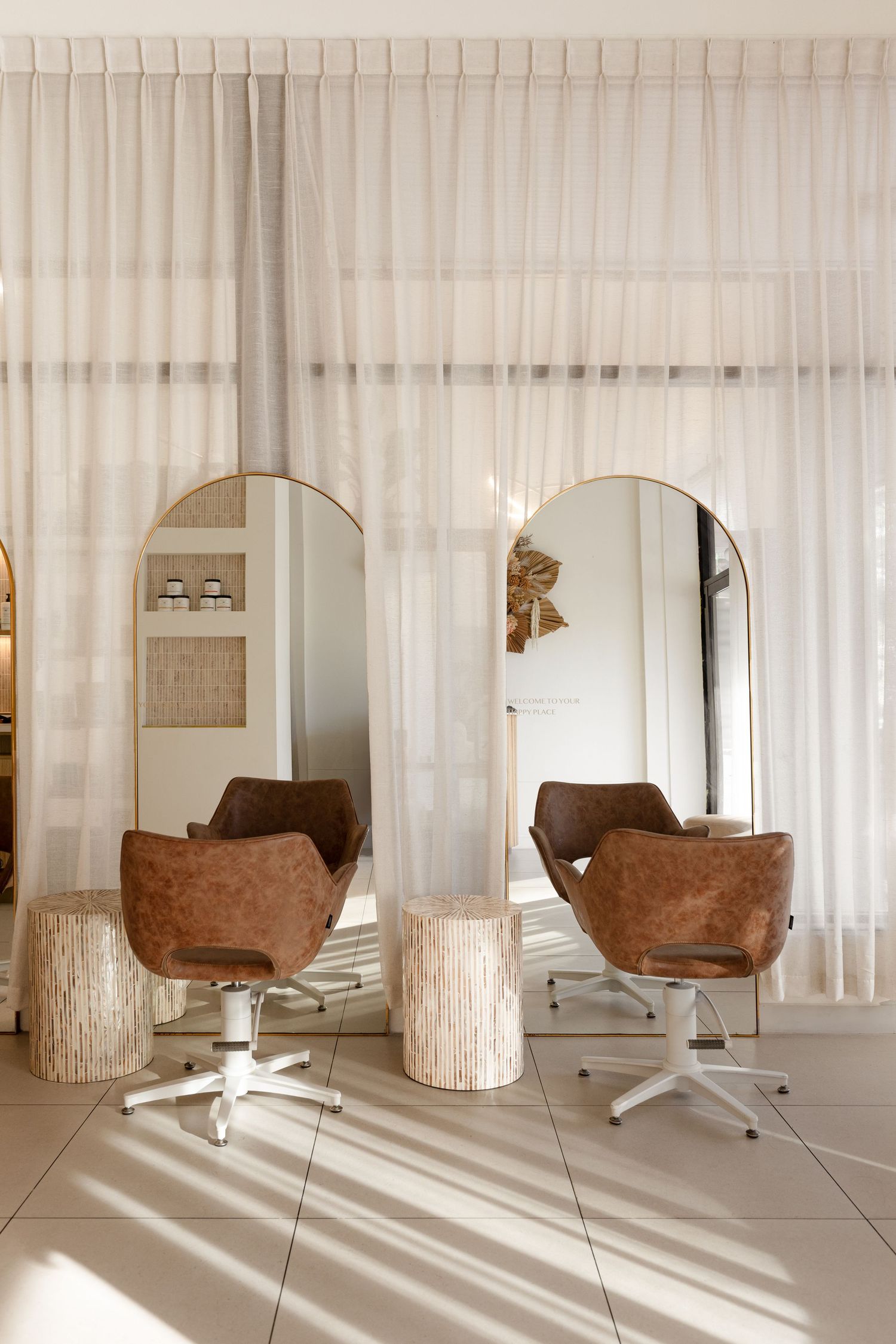 Modern minimalist interior with brown leather chair and sheer white curtains casting dramatic shadows on tiled floor.