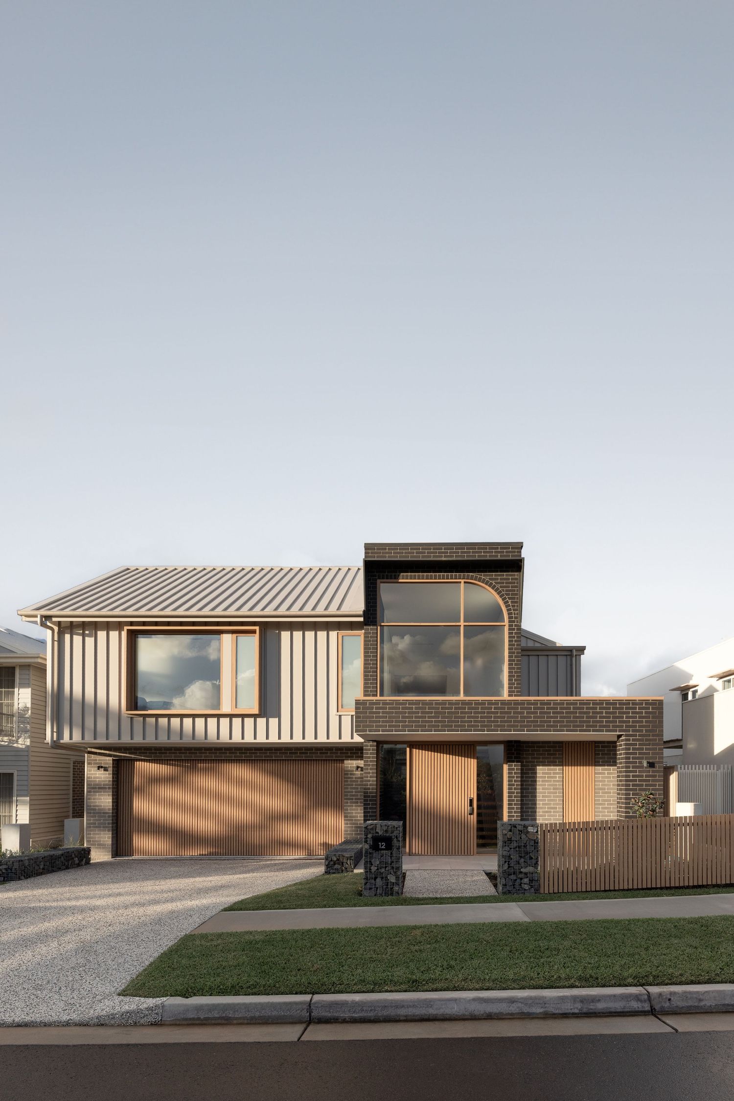 Modern residential home exterior featuring wood cladding, brick accents, and large windows in a contemporary architectural style.