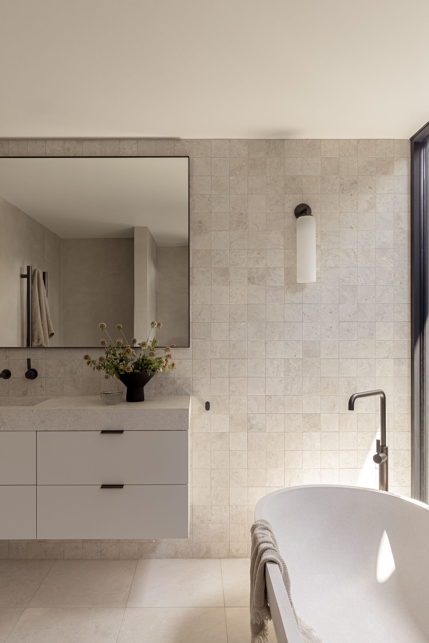 Modern bathroom with white floating vanity, large mirror, freestanding tub, and textured stone tiles.