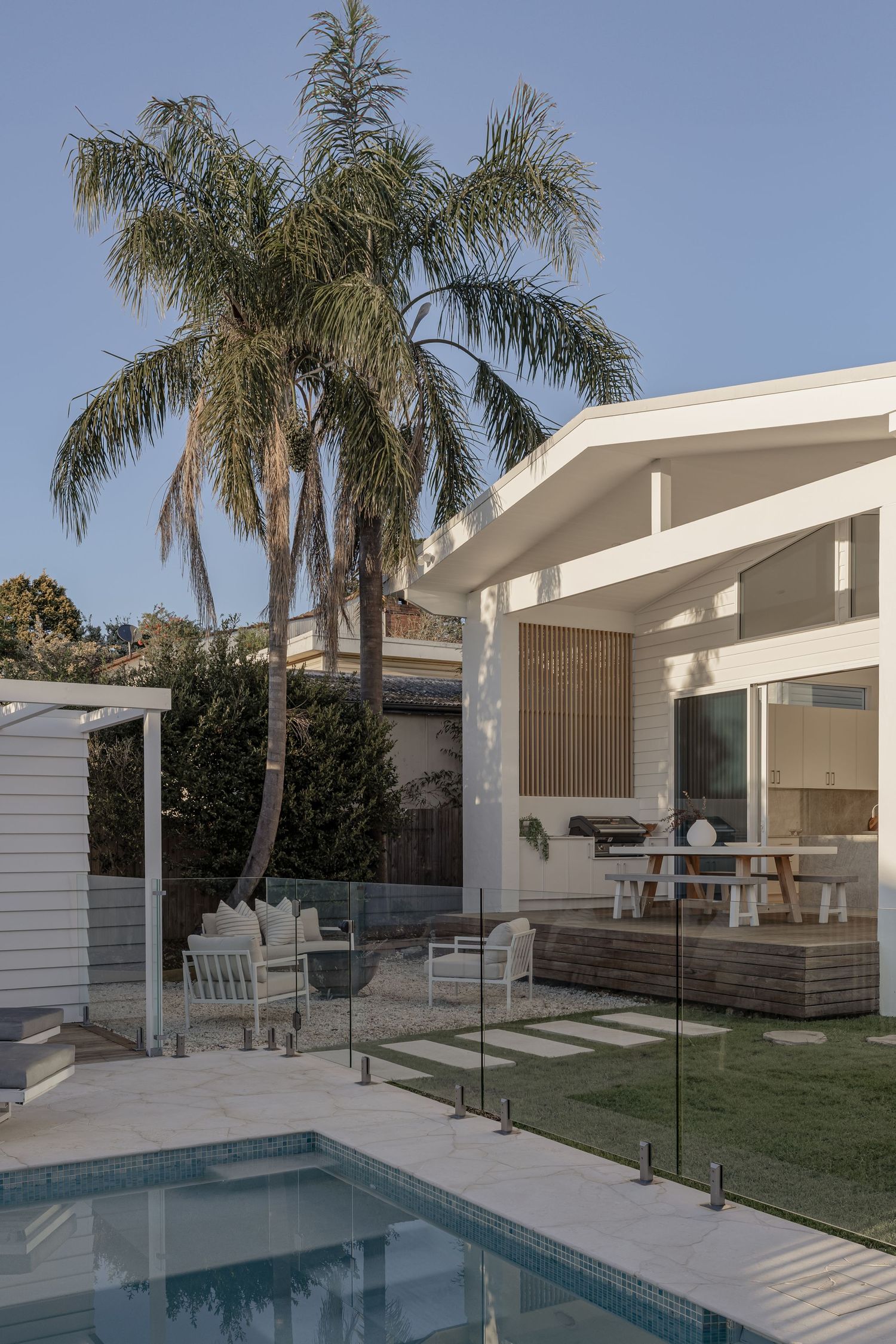 Modern white poolside patio with glass railings and palm trees features clean architectural lines and minimalist design.