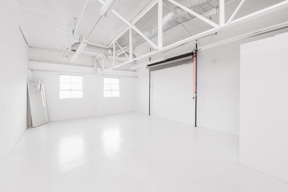 Clean white photography studio space with exposed ceiling beams and natural lighting.