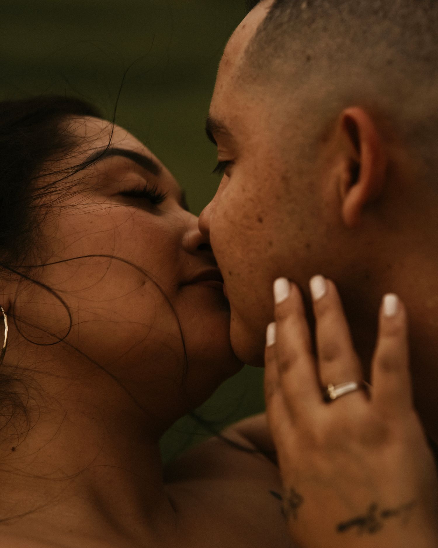 A couple shares an intimate kiss, with the woman's hand gently cradling the man's face, wearing a silver ring.