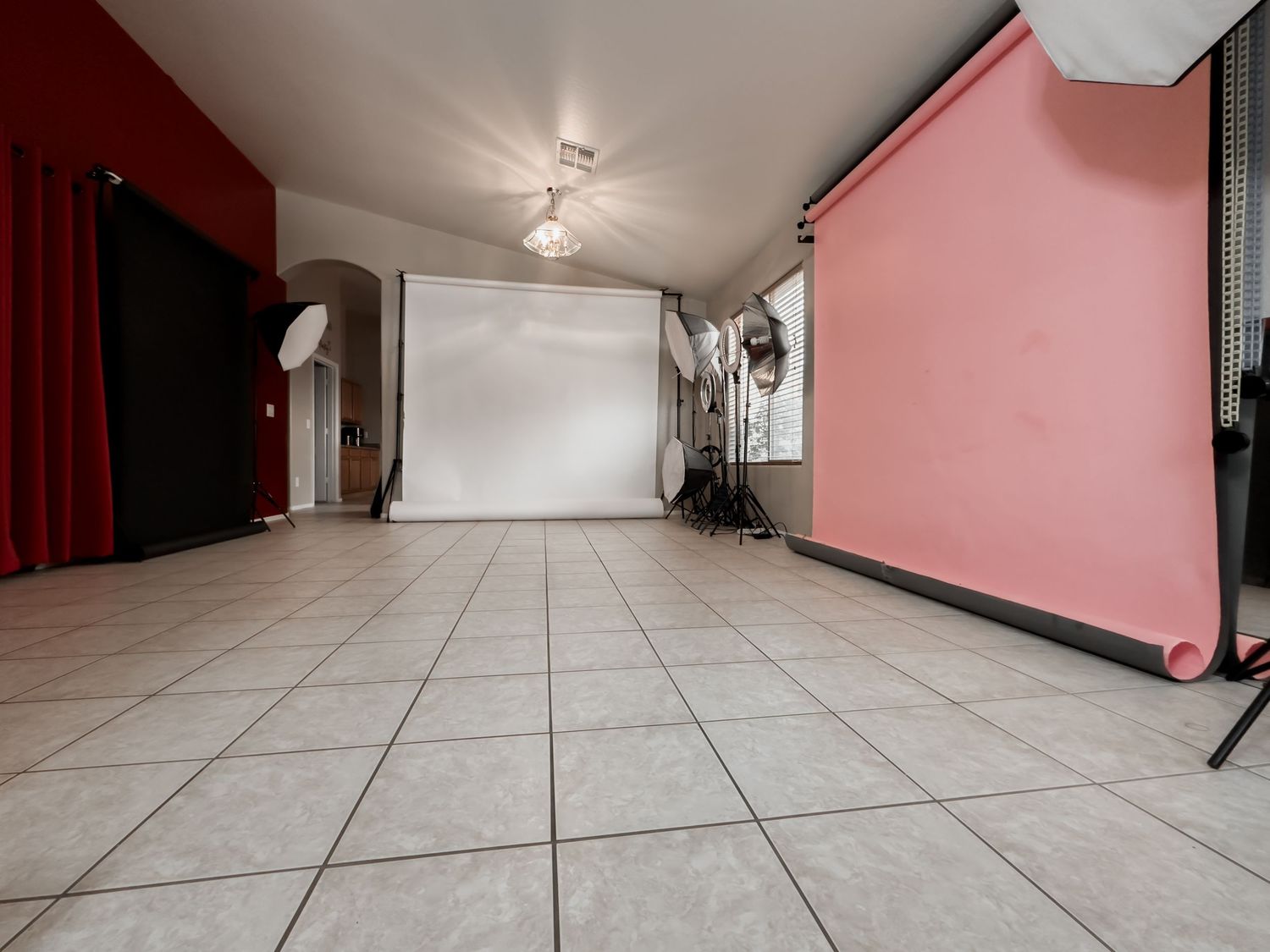Empty photo studio with pink walls, white tile flooring, and professional lighting equipment.