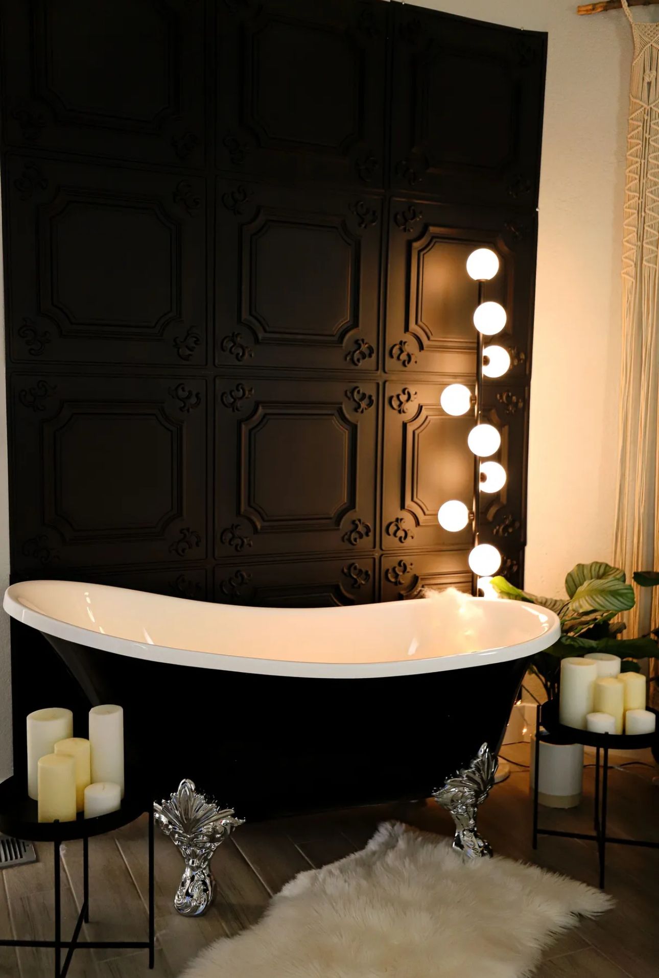 Modern black clawfoot tub with globe lights and decorative wall panels creating dramatic bathroom scene.