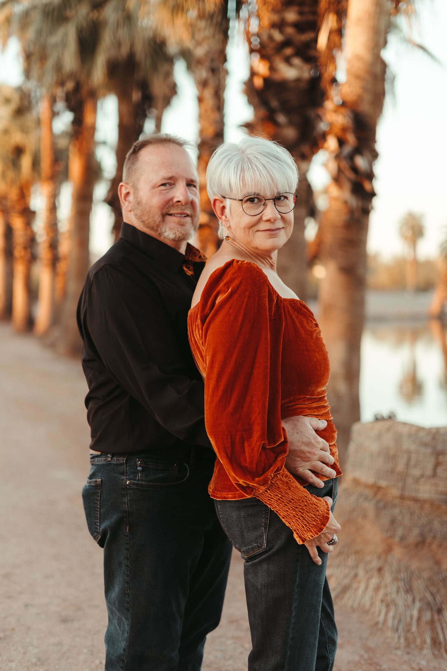 Couple sharing a tender embrace and laughter among palm trees at sunset.