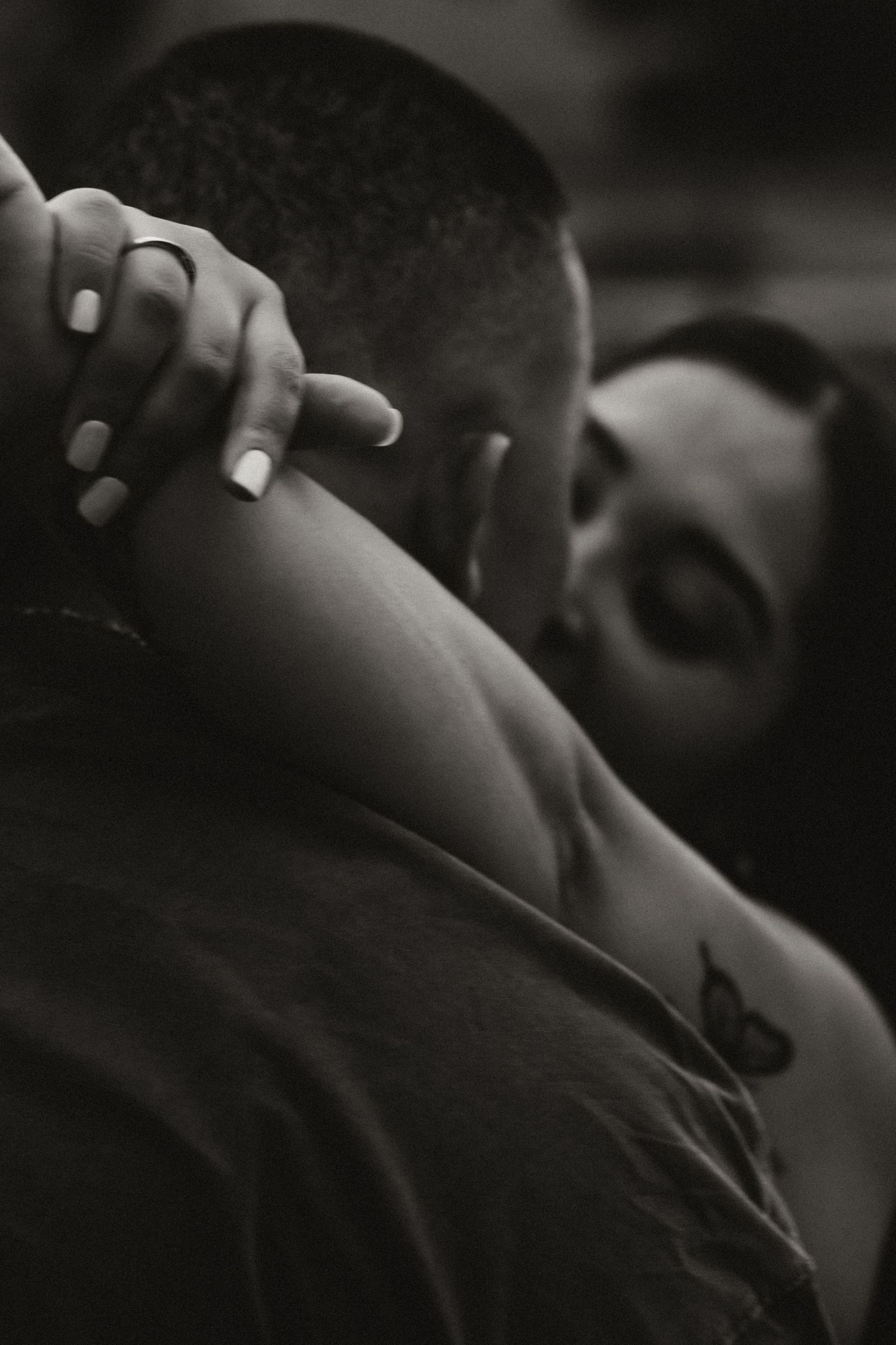Black and white photo of a couple embracing intimately, woman with butterfly tattoo wrapping arms around mans neck.