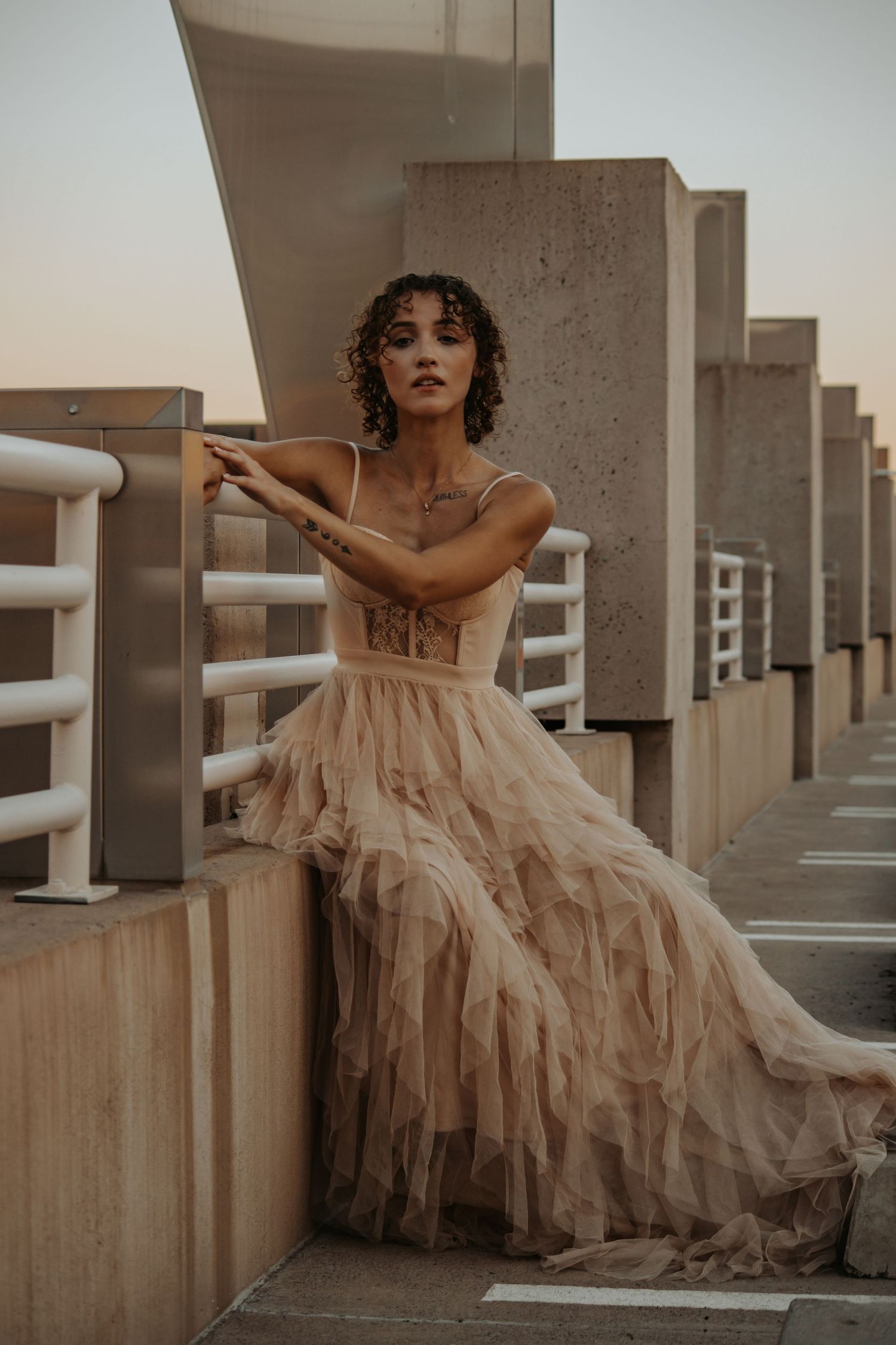 Woman in flowing tulle dress poses dramatically on concrete architecture.
