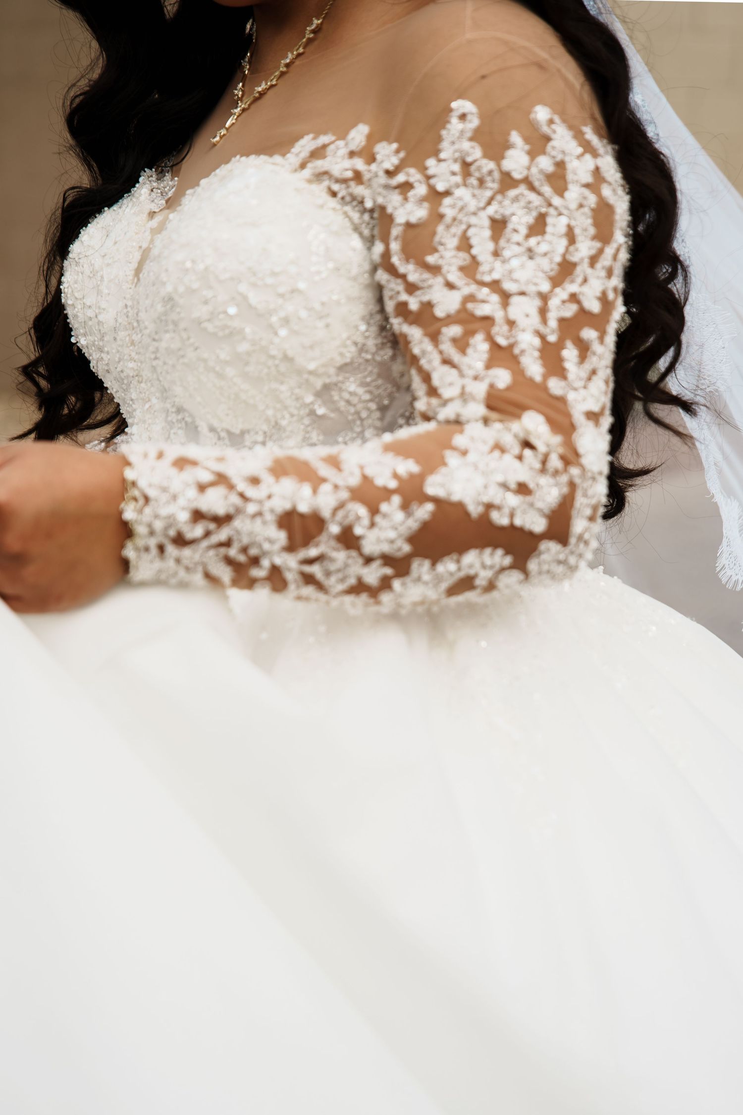 Close-up of a bride wearing an elegant lace long-sleeve wedding gown with intricate floral beading details.