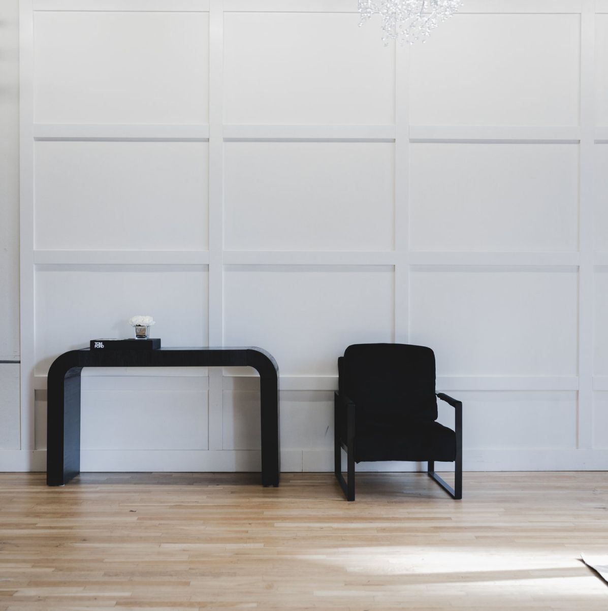 Minimalist interior with black console table and chair against white paneled wall.