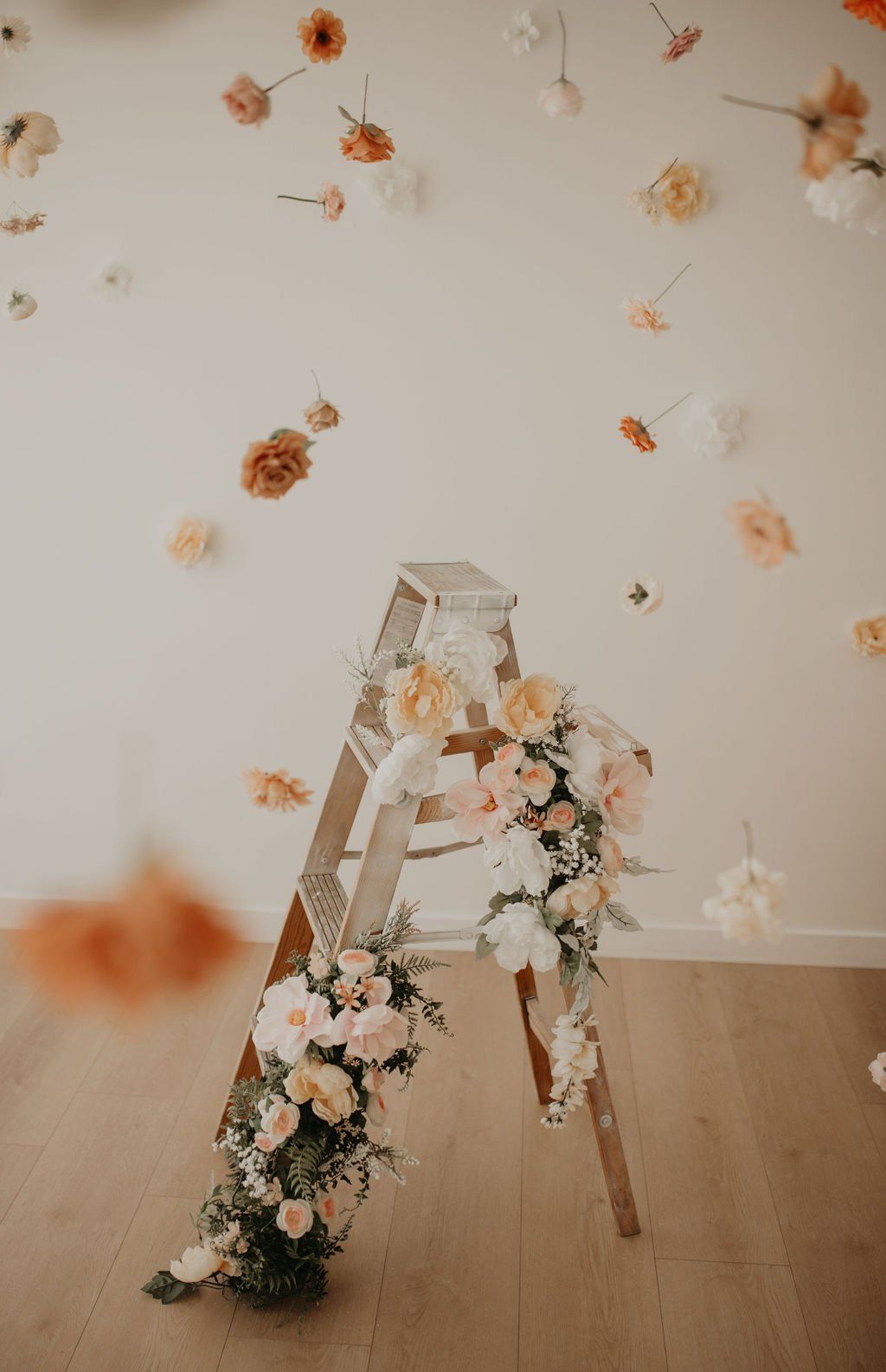 Vintage wooden ladder decorated with delicate peach and white flowers against light wall.